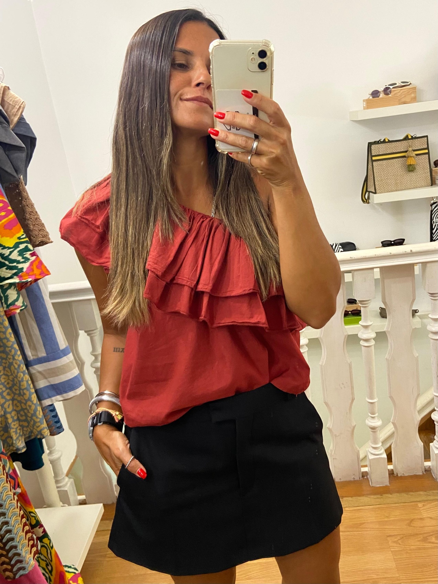 Mulher com blusa vermelha de folhos e saia preta numa selfie em espelho