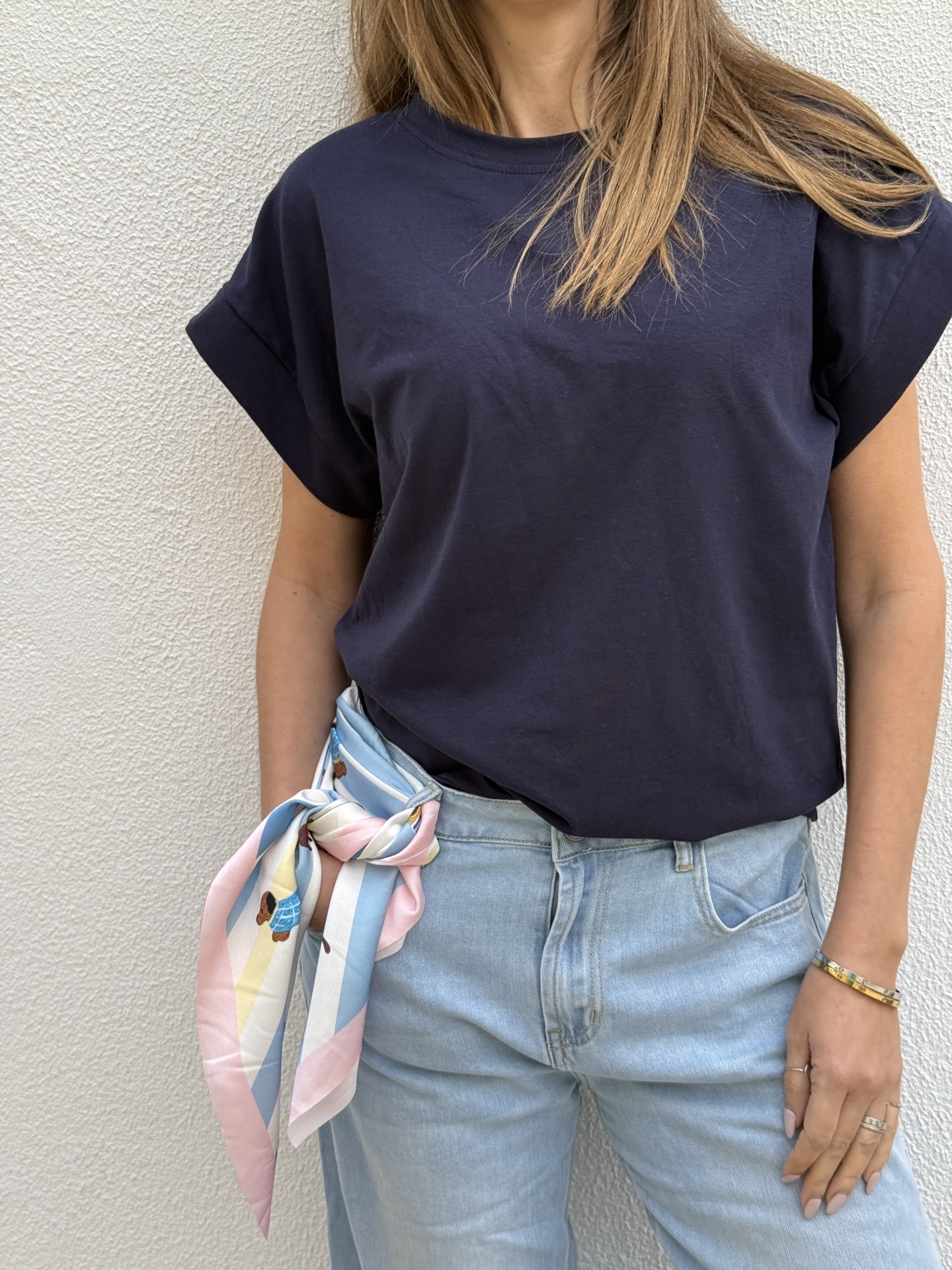 Pessoa com t-shirt azul escura, jeans claros e lenço colorido na cintura