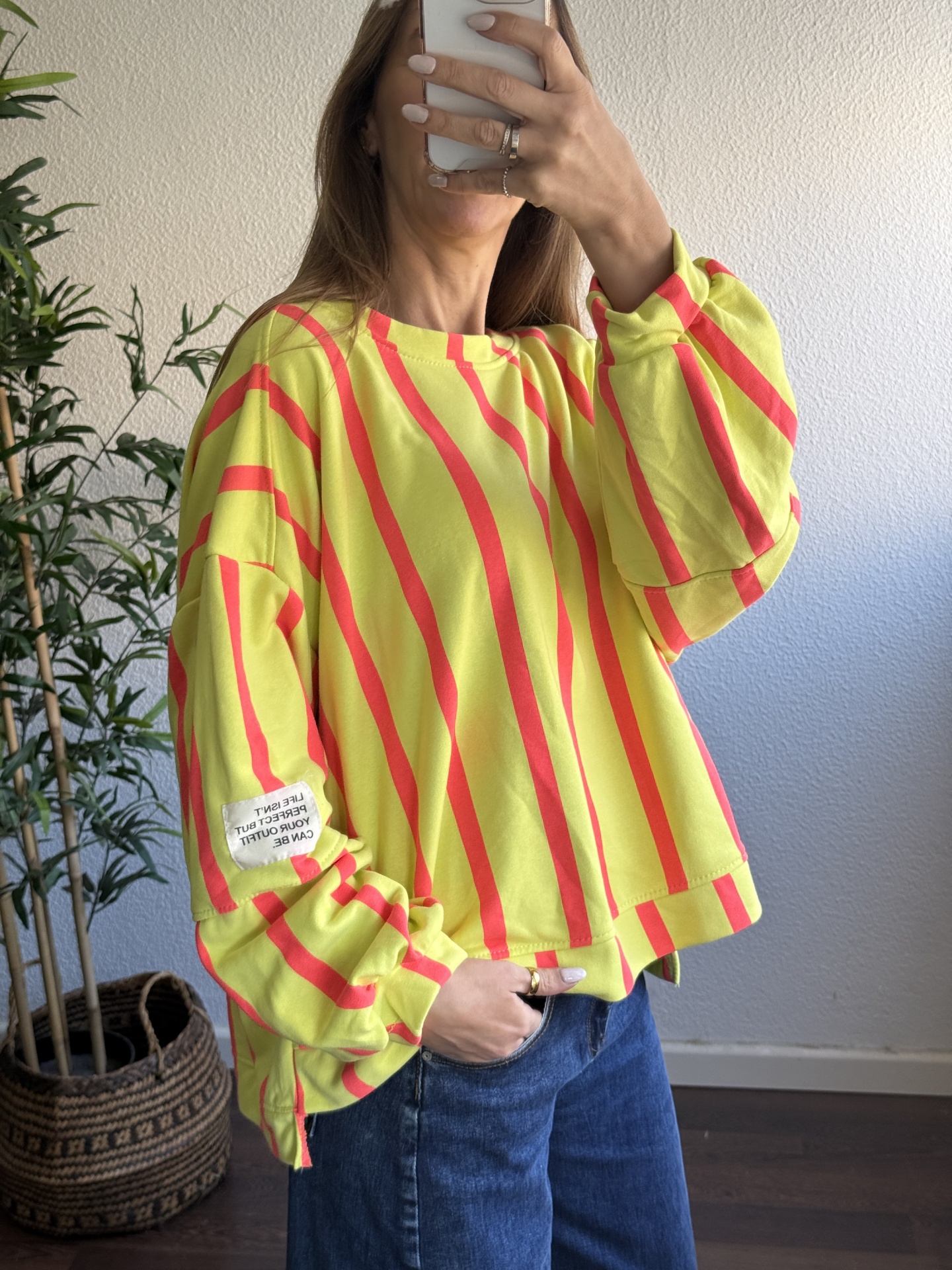 Sweatshirt amarela com riscas vermelhas e etiqueta na manga, usada com jeans azul