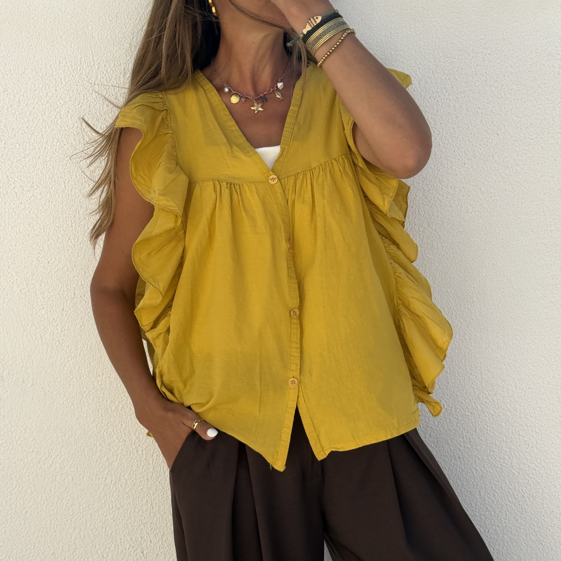 Blusa amarela com botões e folhos nas mangas usada com calças pretas e acessórios