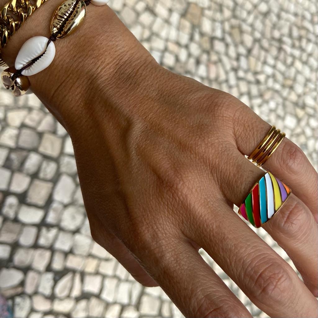 Mão com pulseiras de conchas e anel colorido sobre calçada portuguesa