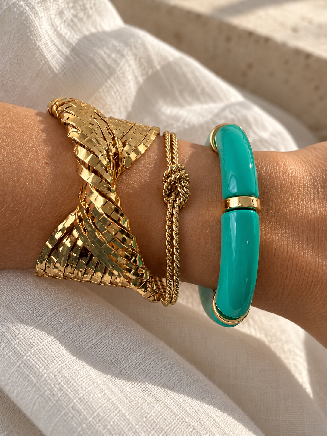 Pulseiras douradas e azul turquesa numa mão com fundo de tecido branco