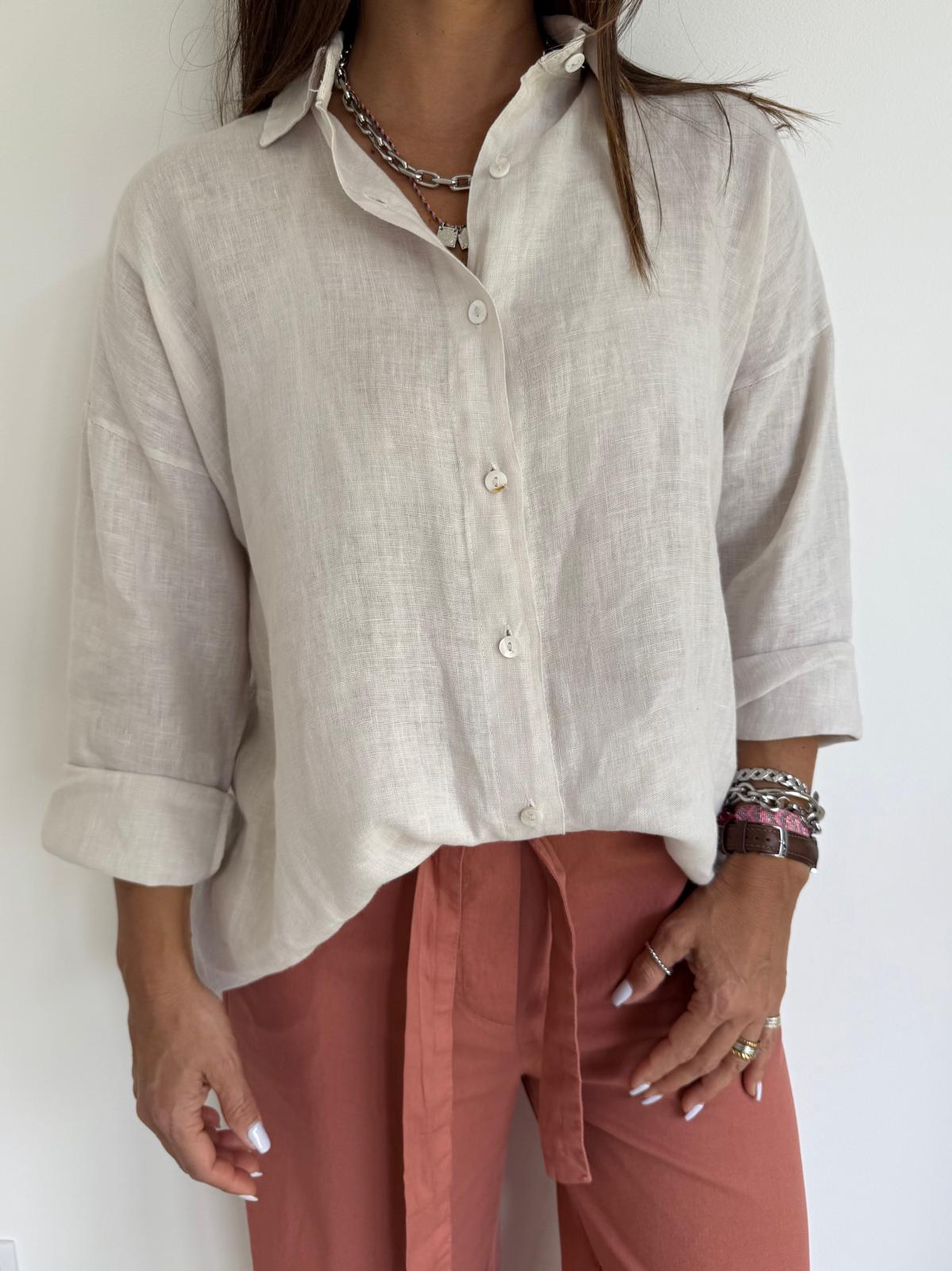Camisa branca de linho com botões e mangas arregaçadas, calças cor de tijolo com cinto e pulseiras no pulso