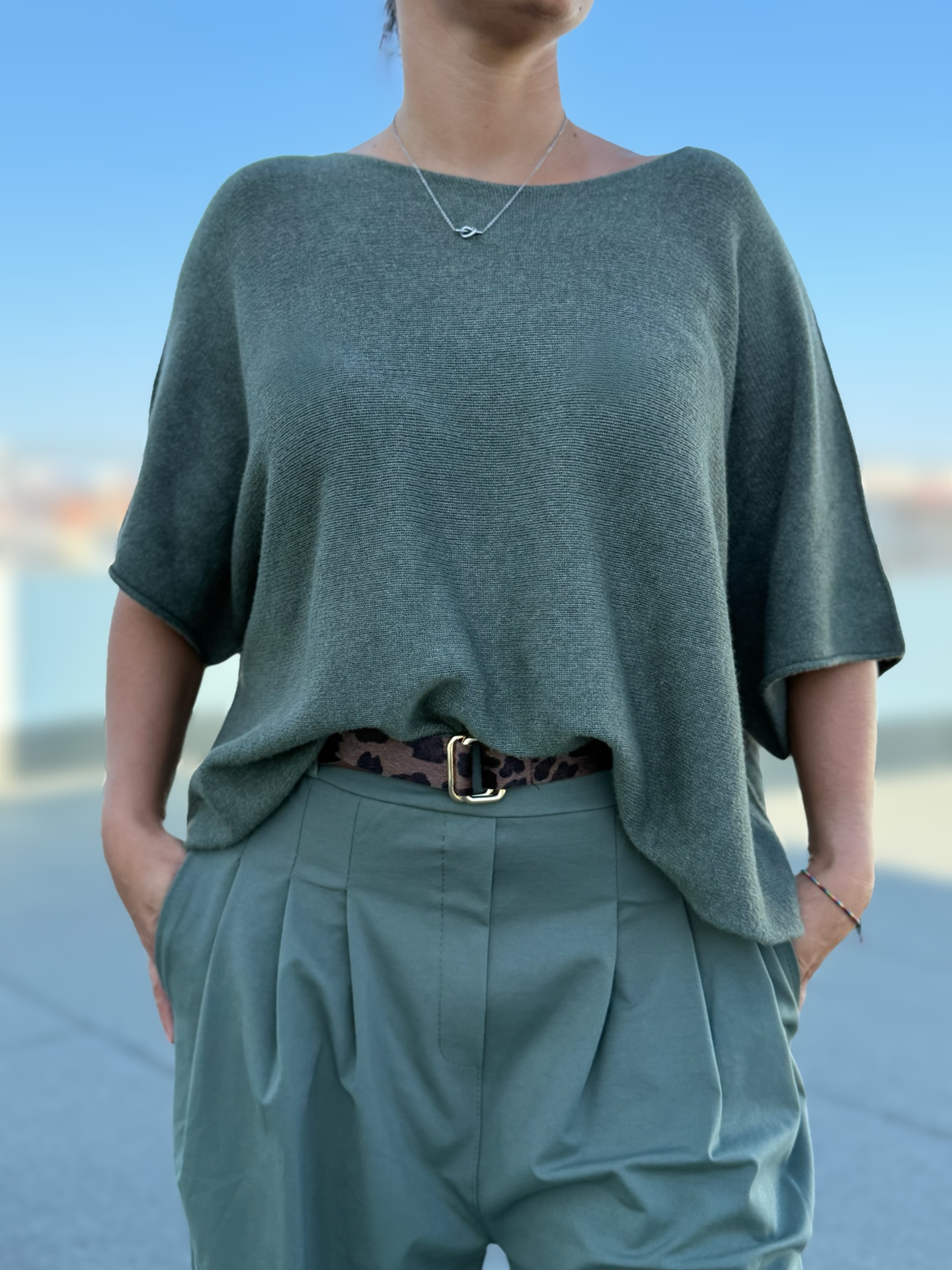 Pessoa vestindo sweater cinzento, calças verdes e cinto com padrão animal print