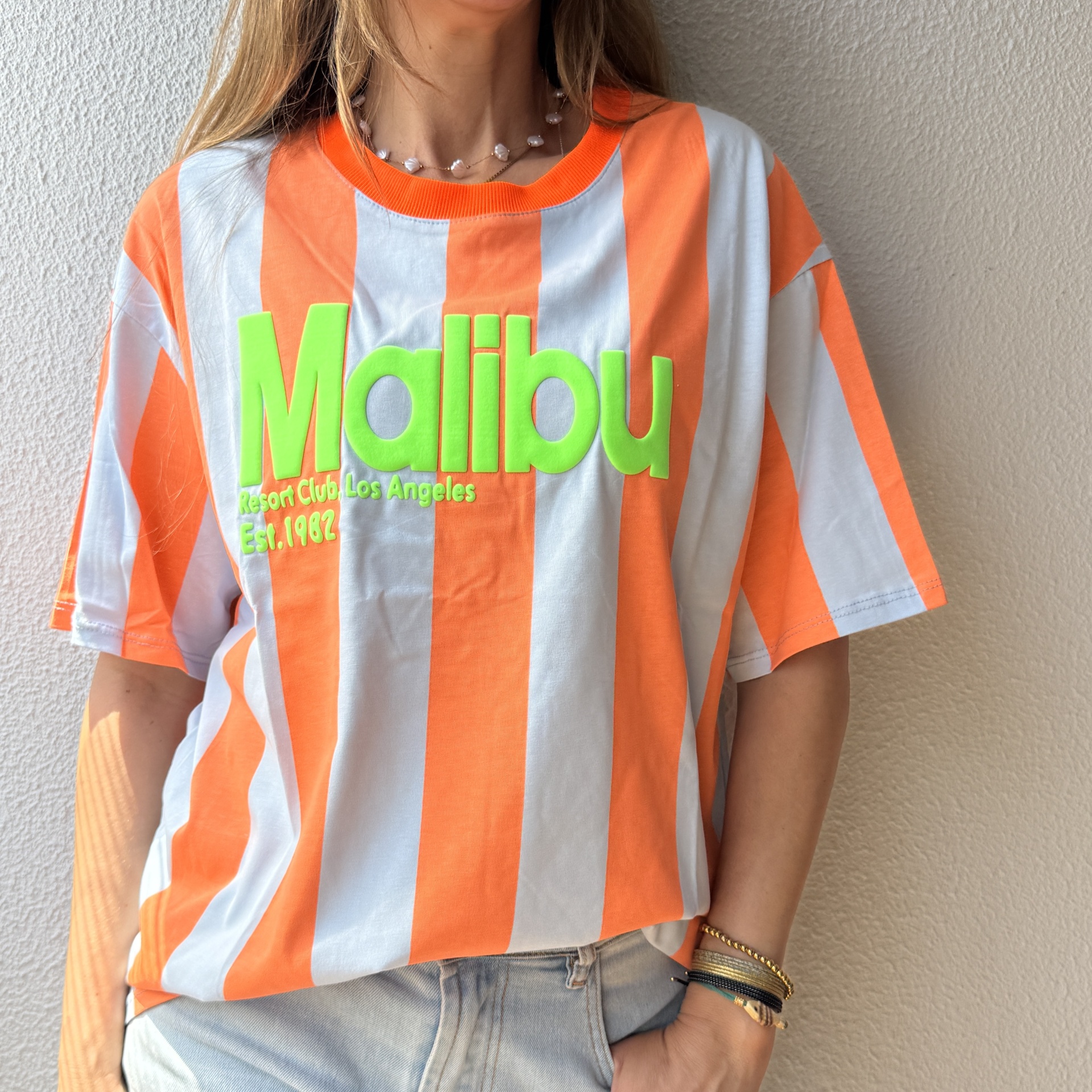 T-shirt riscada laranja e branca com texto verde MALIBU e jeans azuis