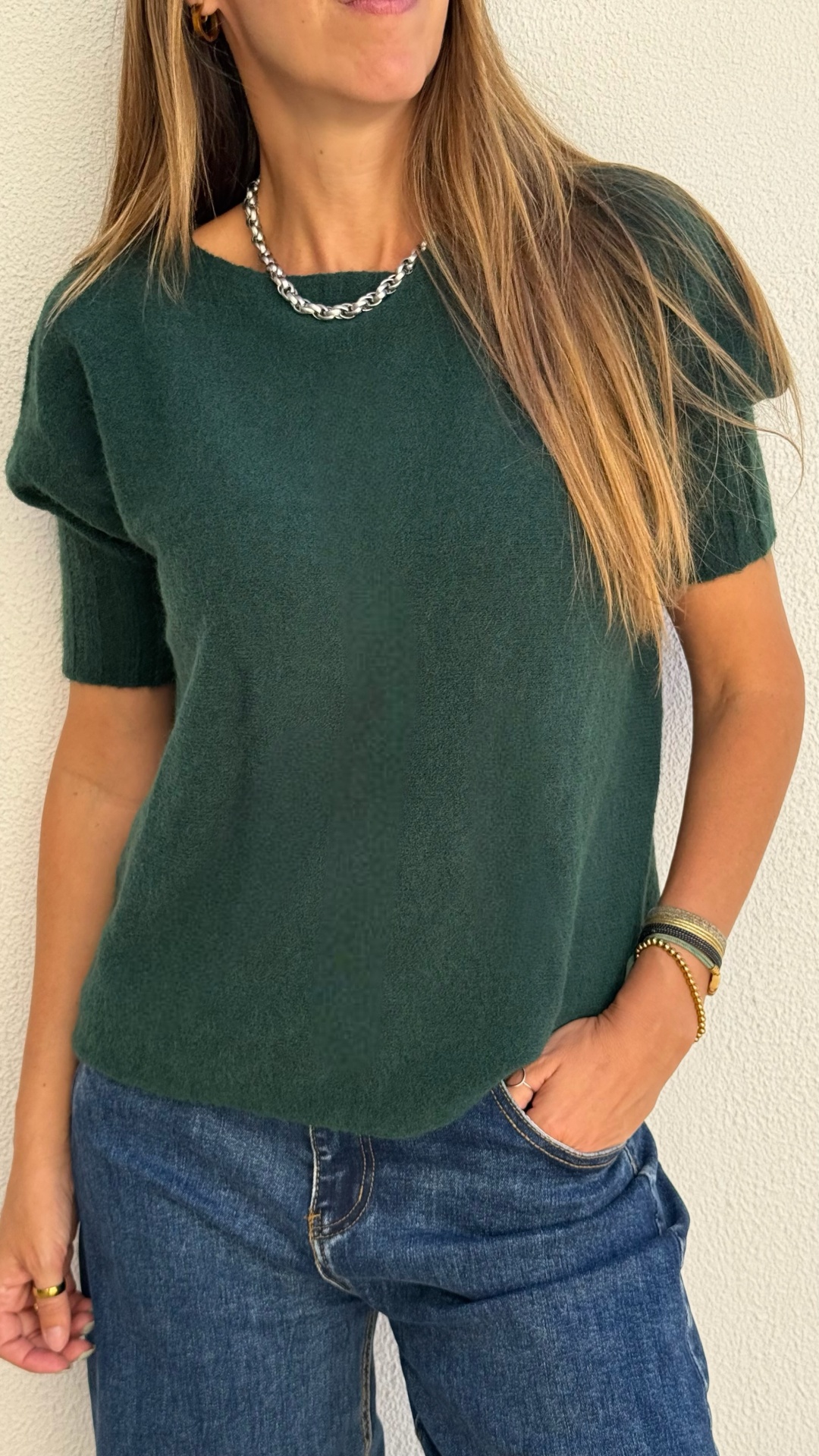 Camisola de malha verde escuro com mangas curtas e jeans azuis.