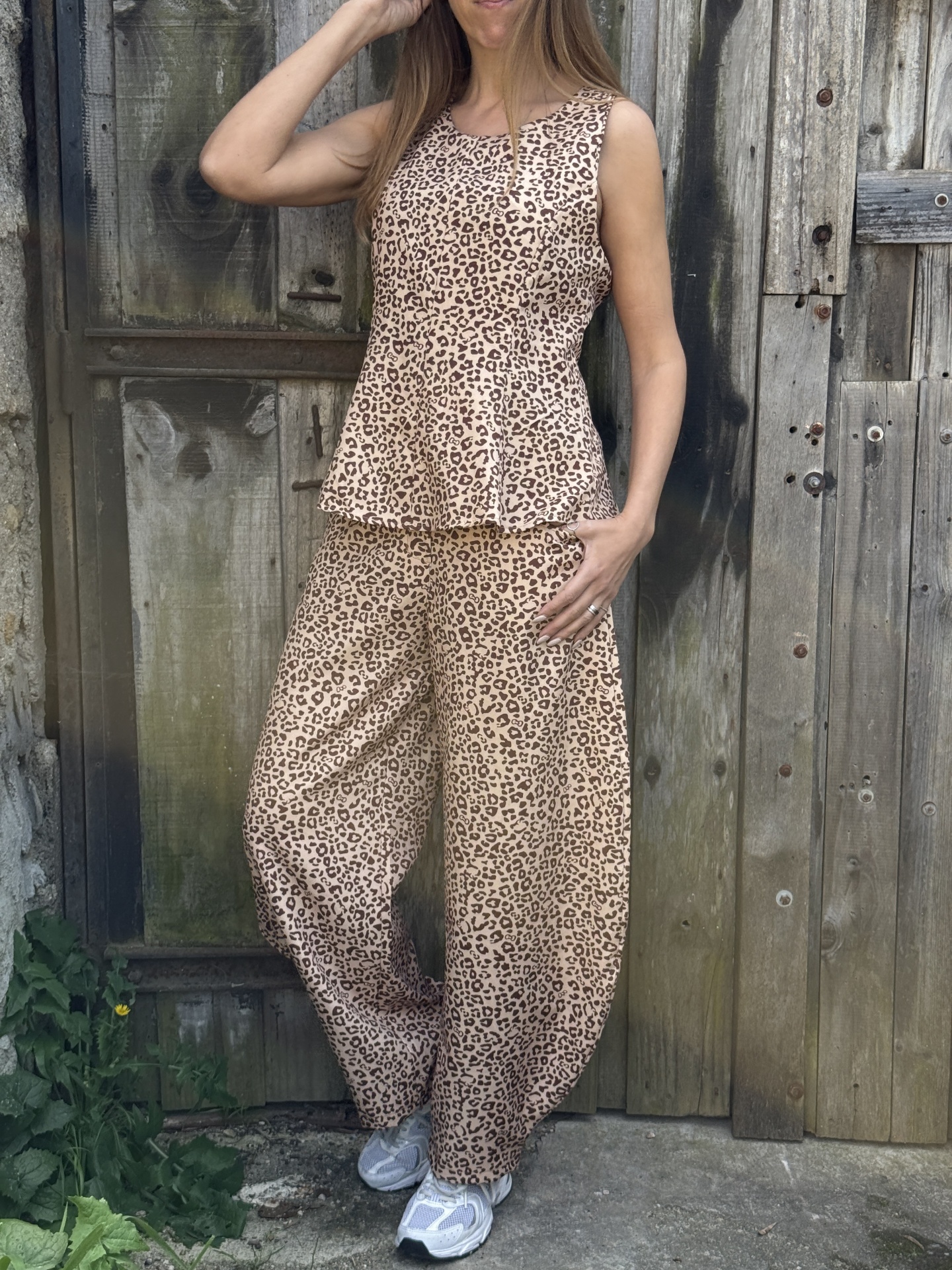 Mulher com conjunto animal print bege e castanho com sapatilhas brancas em frente a porta de madeira antiga