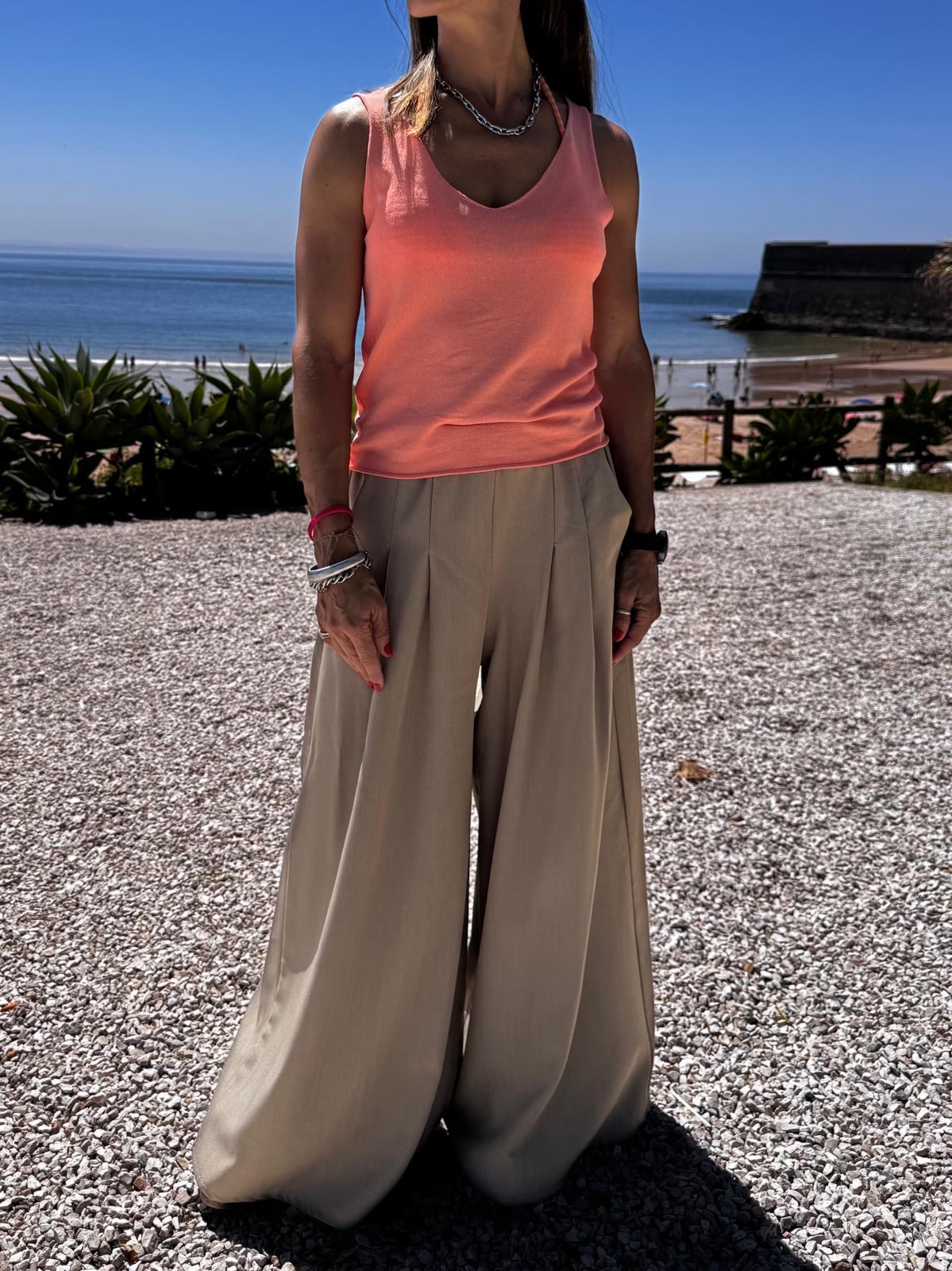 Mulher vestindo regata salmão e calças largas beges na praia