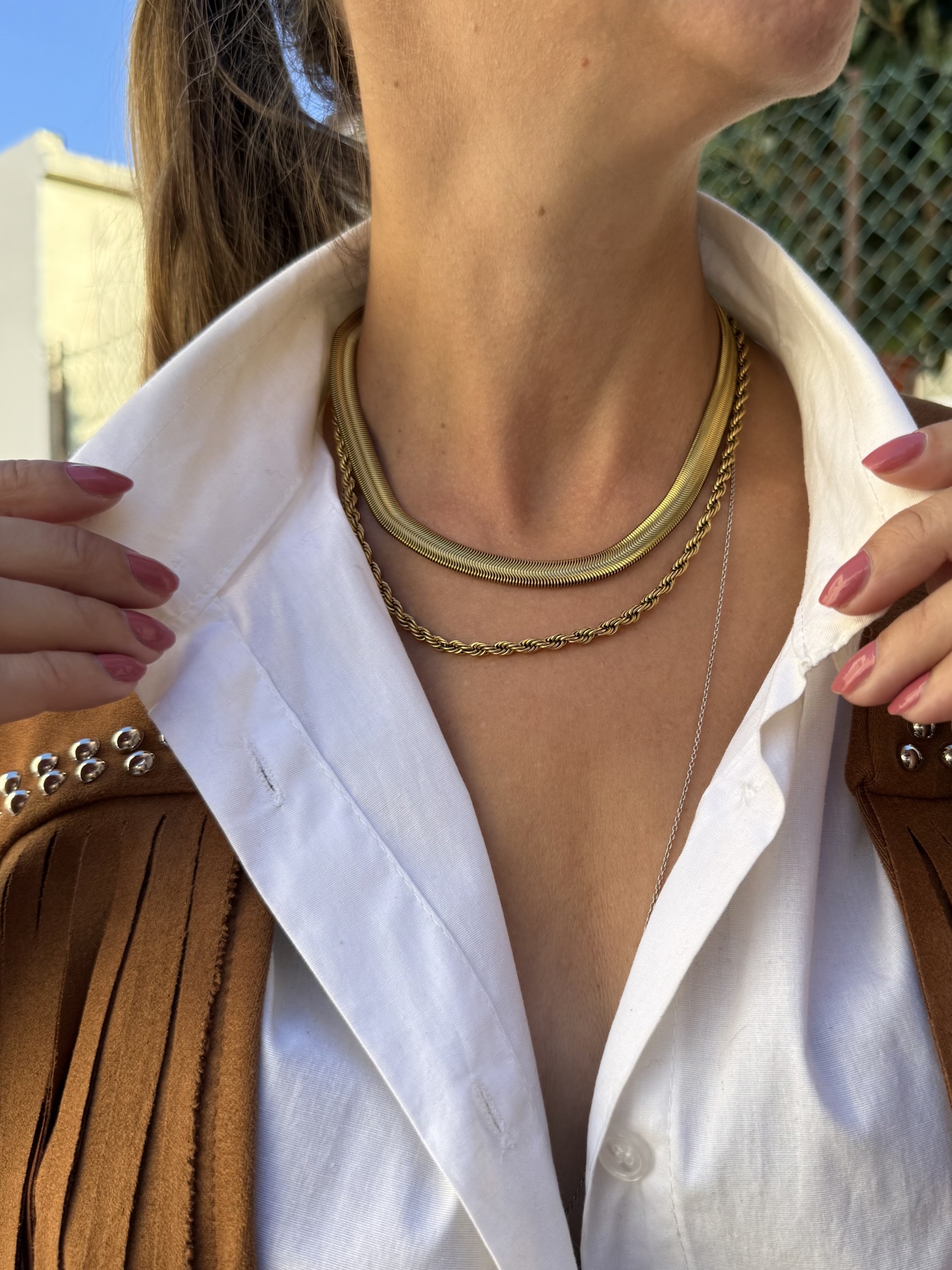 Colar dourado de três correntes usadas com camisa branca e casaco castanho