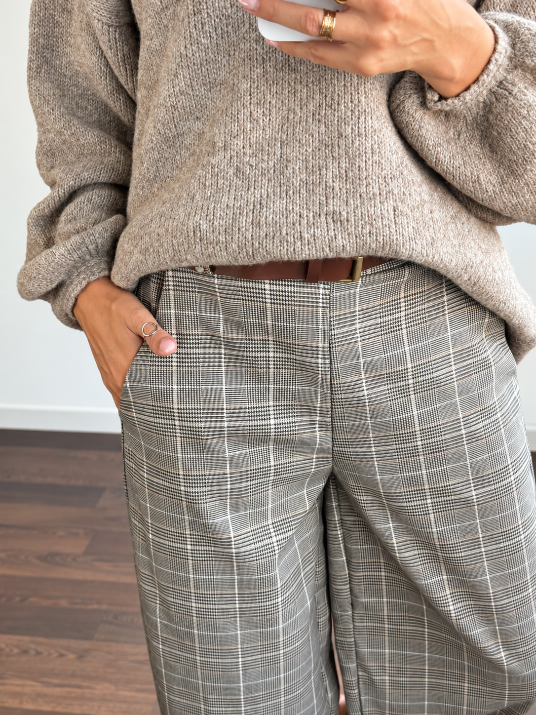 Pessoa com camisola castanha de malha e calças padrão príncipe de gales com cinto castanho