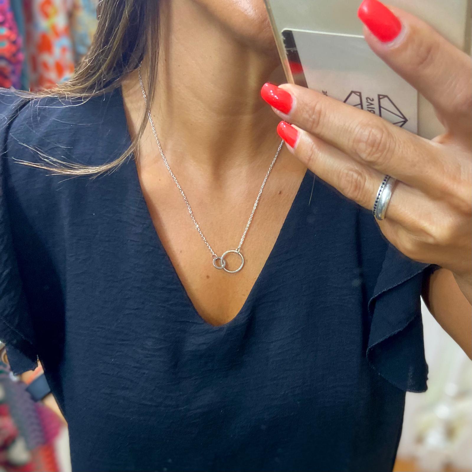 Colar prateado com pendente de círculos em pessoa com camisola preta e unhas vermelhas