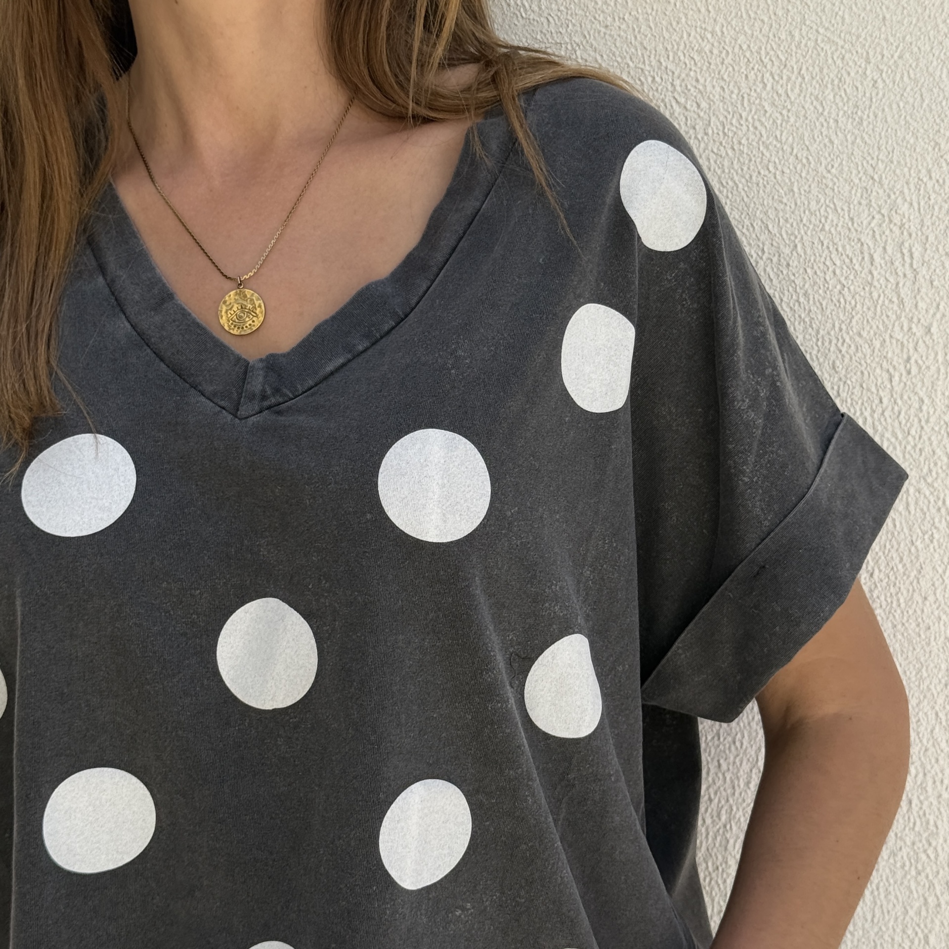 T-shirt cinzenta com bolinhas brancas e colar dourado com pendente redondo em forma de olho.