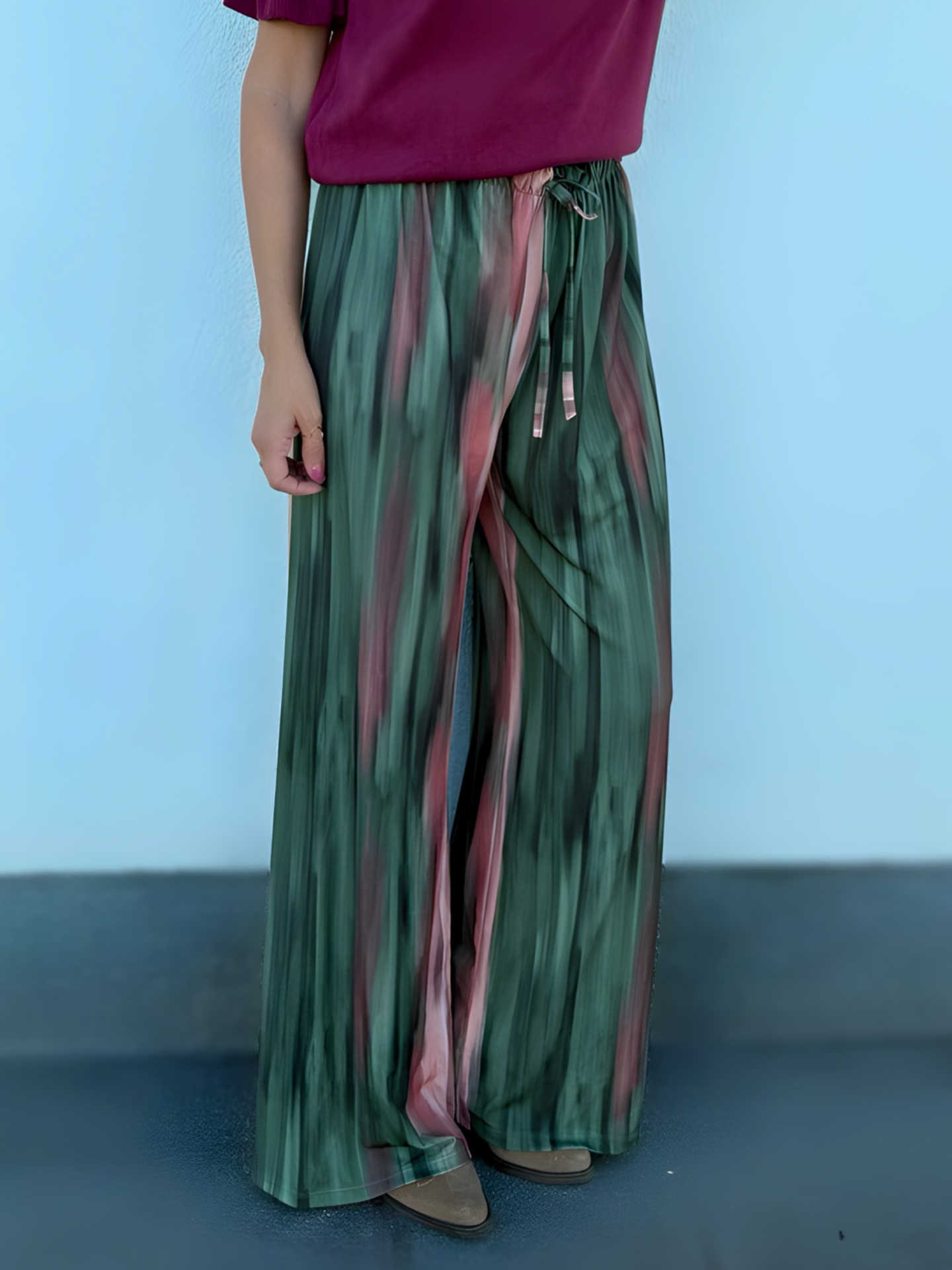 Calças largas em padrões verdes e rosa com cordão na cintura, usadas com blusa vinho e sapatos cinza.