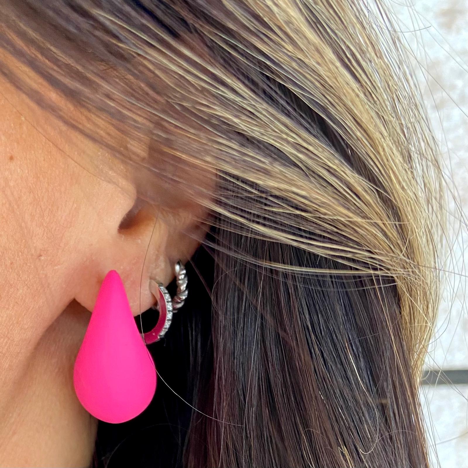 Brinco pendente gota rosa numa orelha com cabelo castanho e loiro