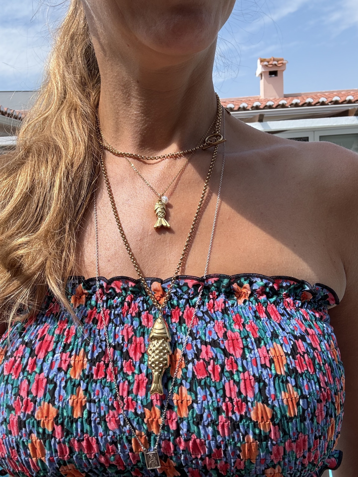 Colares dourados com pingentes de peixe e objeto pequeno em mulher com blusa tomara que caia colorida