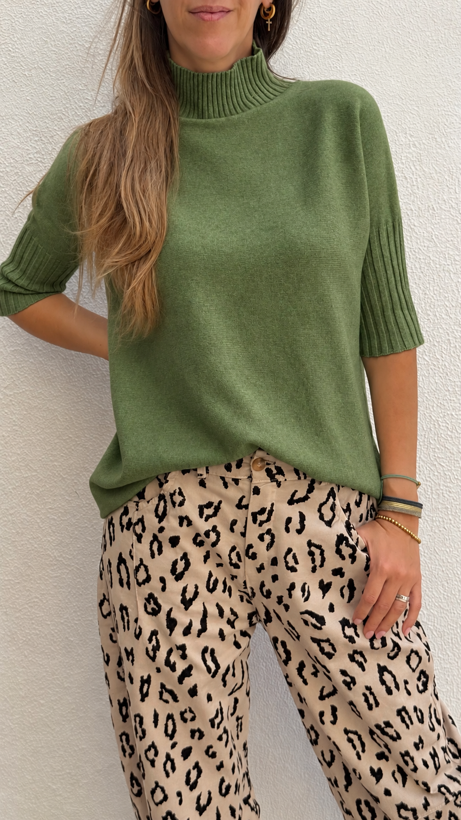 Mulher com camisola verde de gola alta e calças com padrão de leopardo
