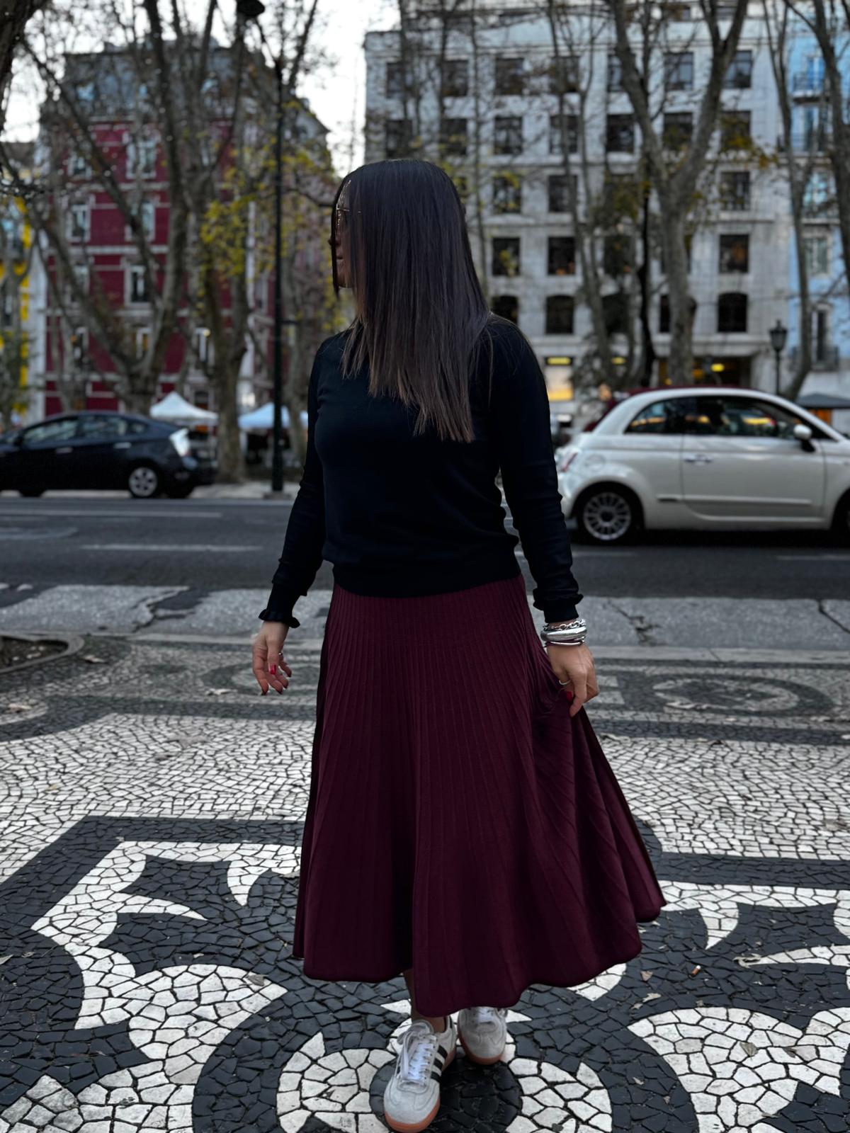 Mulher com saia plissada vinho e camisola preta em calçada portuguesa padrão preto e branco