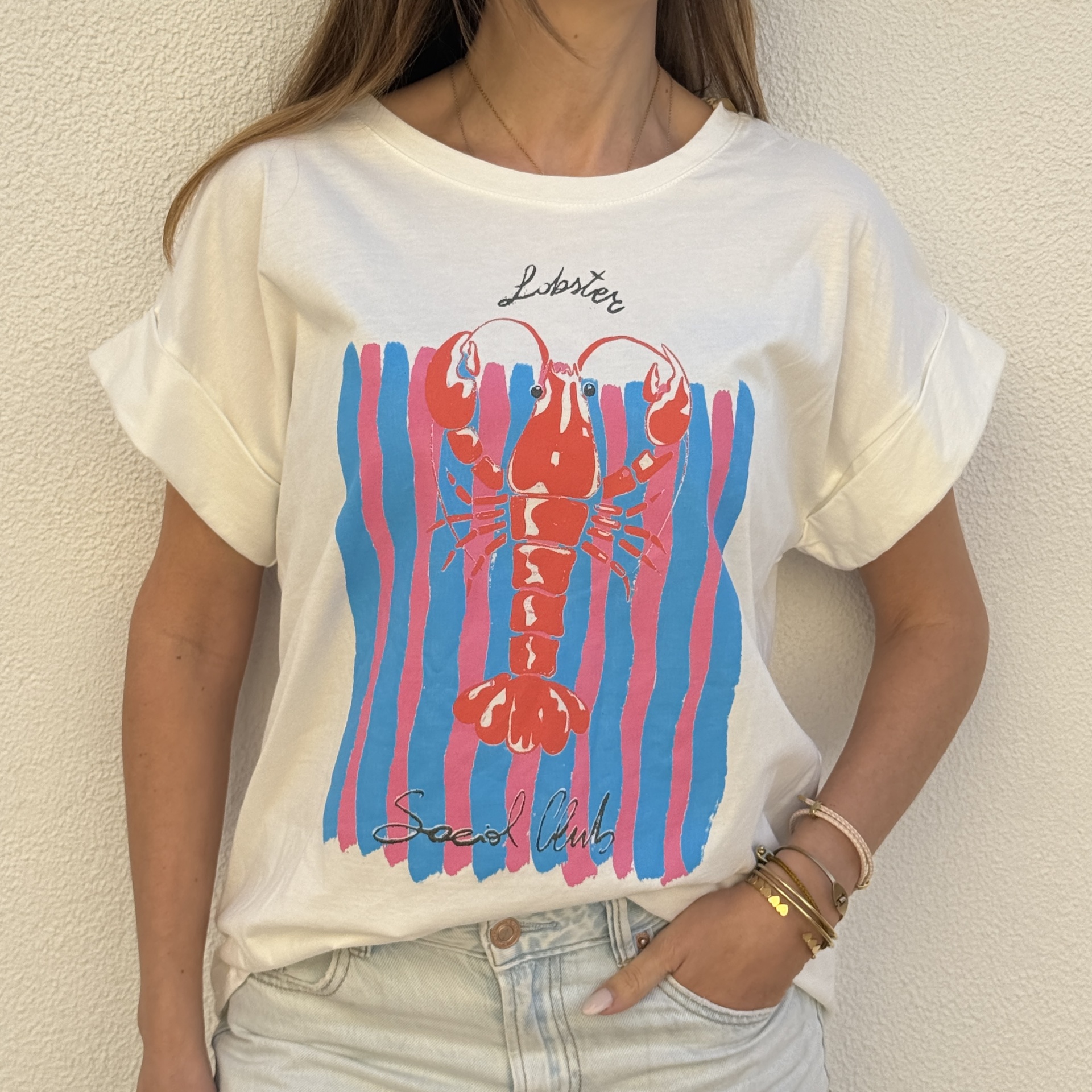 T-shirt branca com estampa de lagosta e riscas coloridas, usada com calças claras
