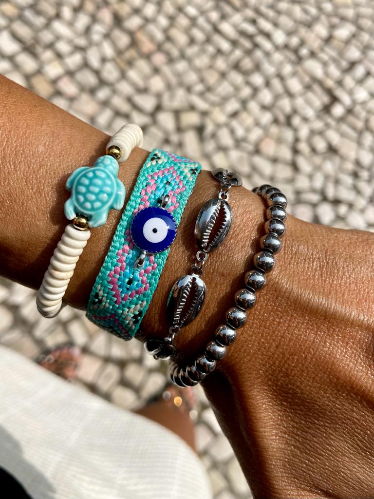 Pulseiras coloridas e metálicas num pulso com fundo de calçada de pedras pequenas