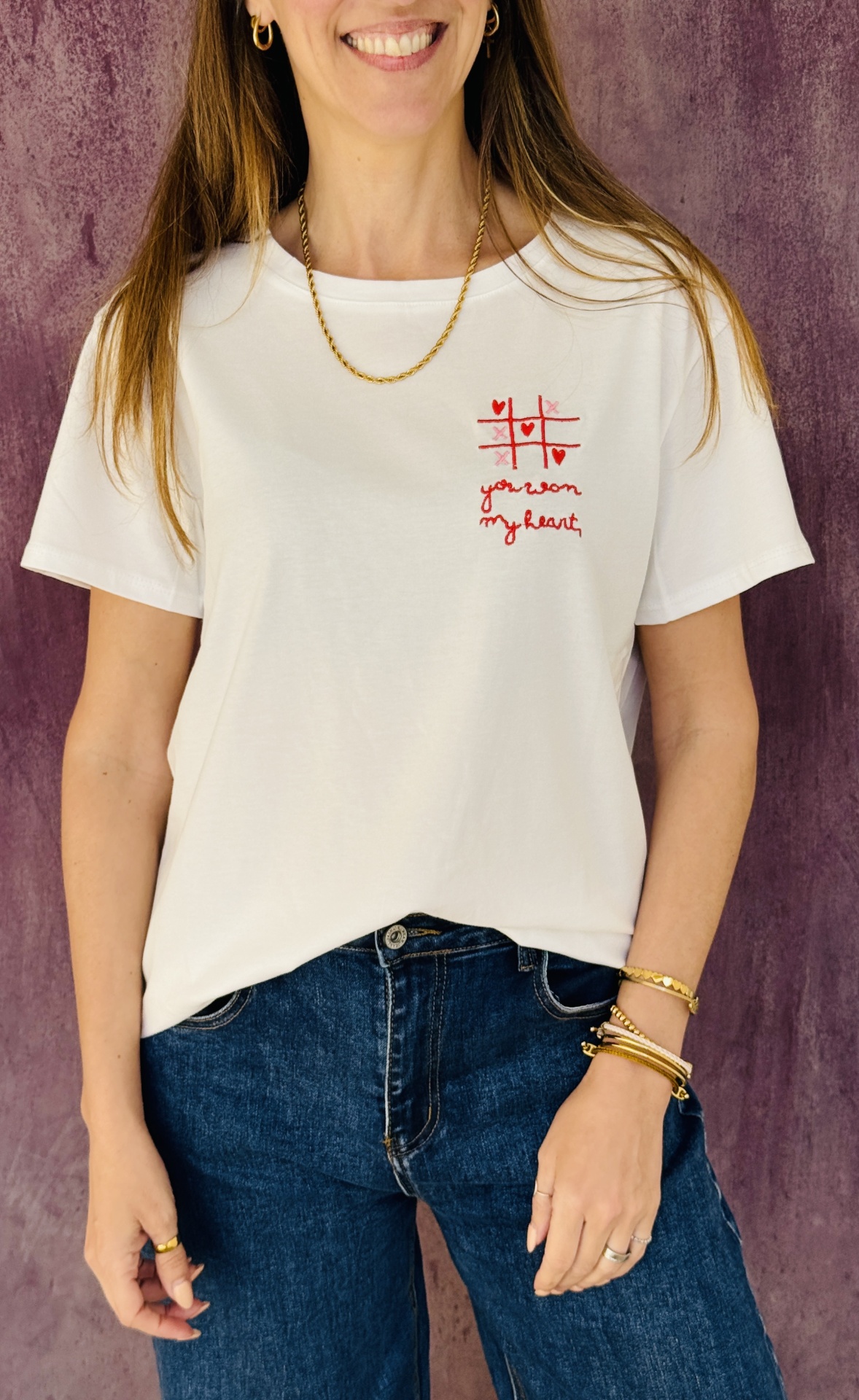 T-shirt branca com bordado vermelho e calças de ganga azuis em fundo roxo