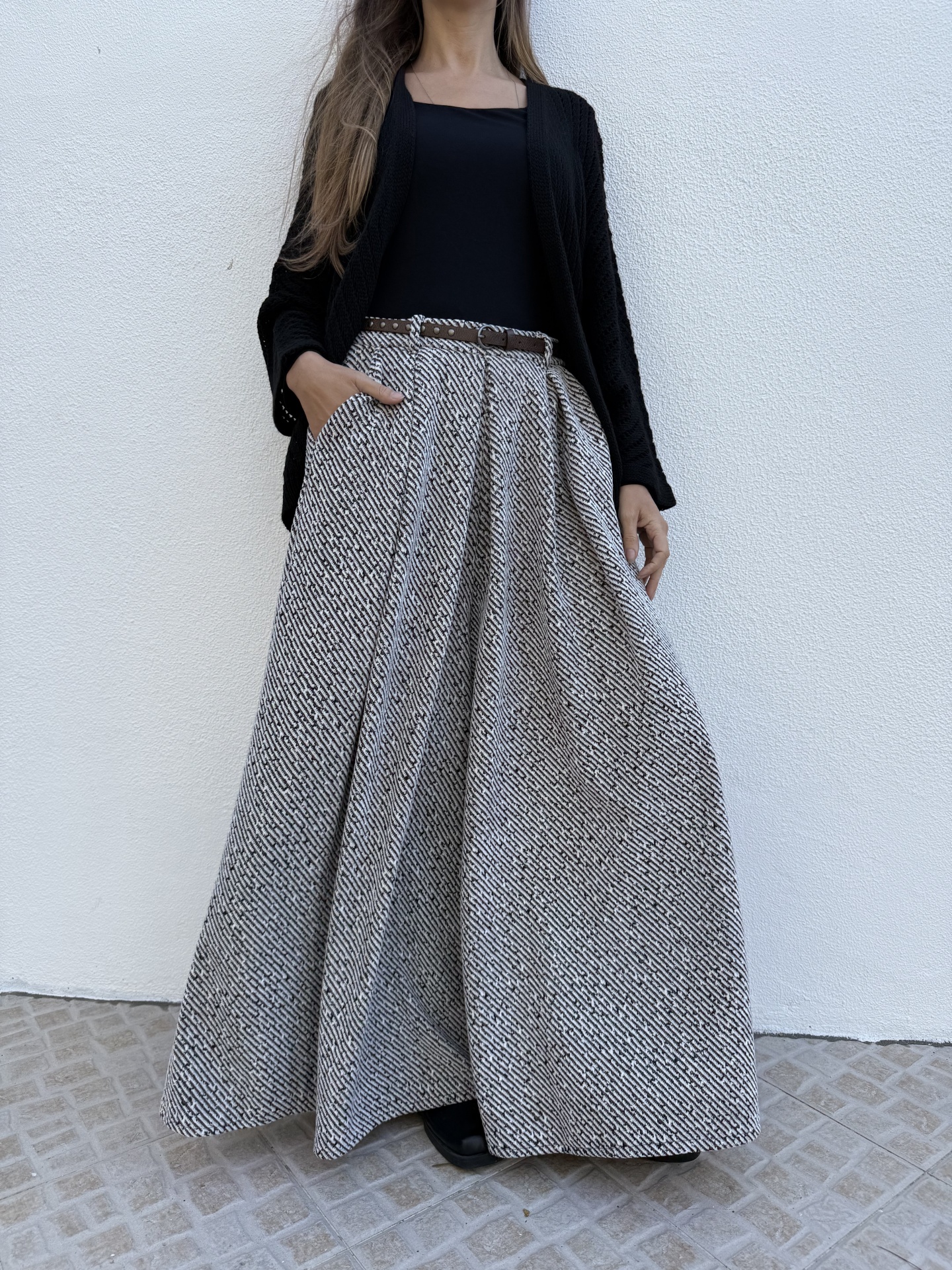 Saia comprida preta e branca com padrão geométrico, cinto castanho, top preto e cardigan preto