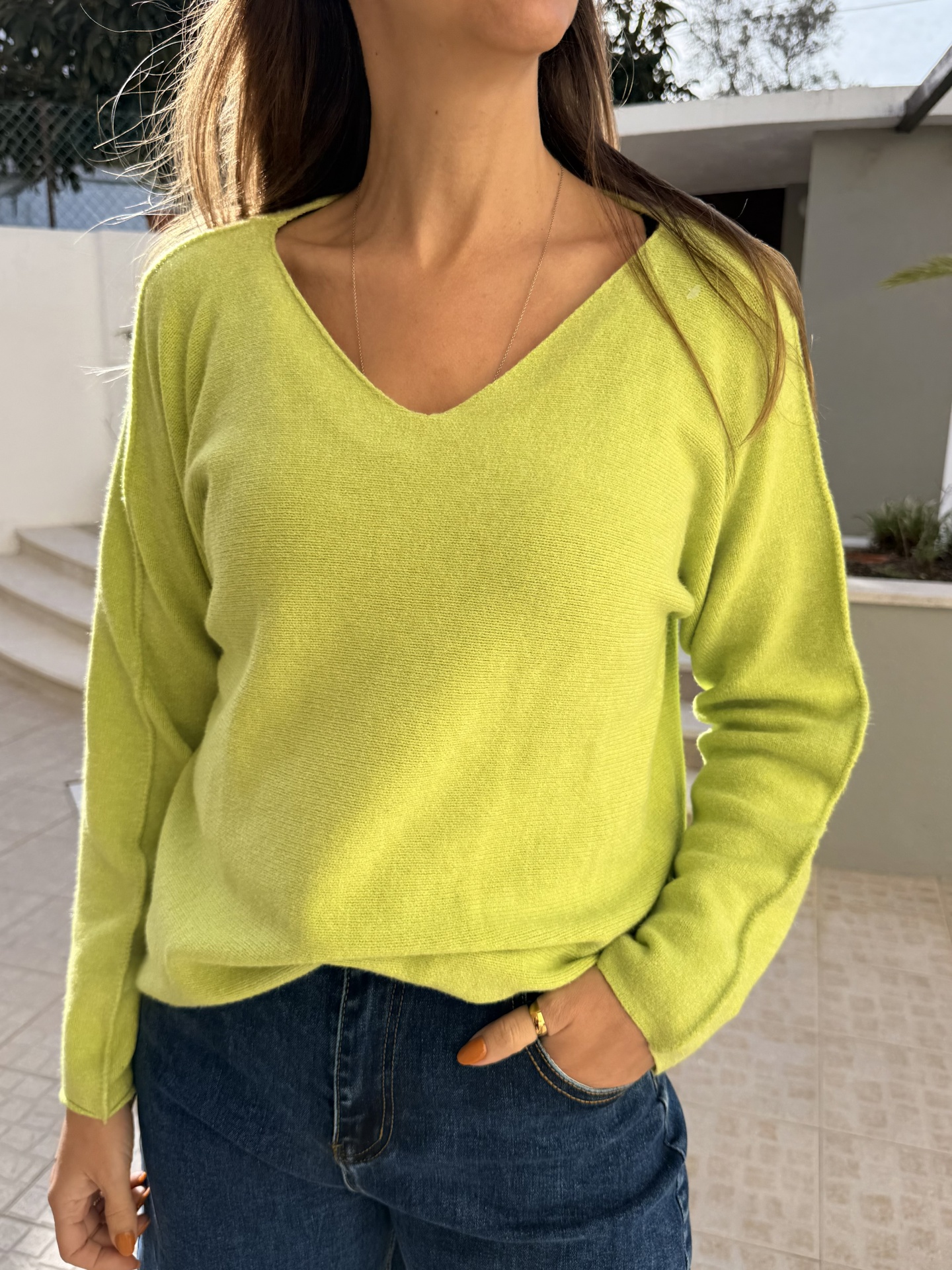Camisola de malha verde lima com decote em V e calças de ganga azuis em ambiente exterior
