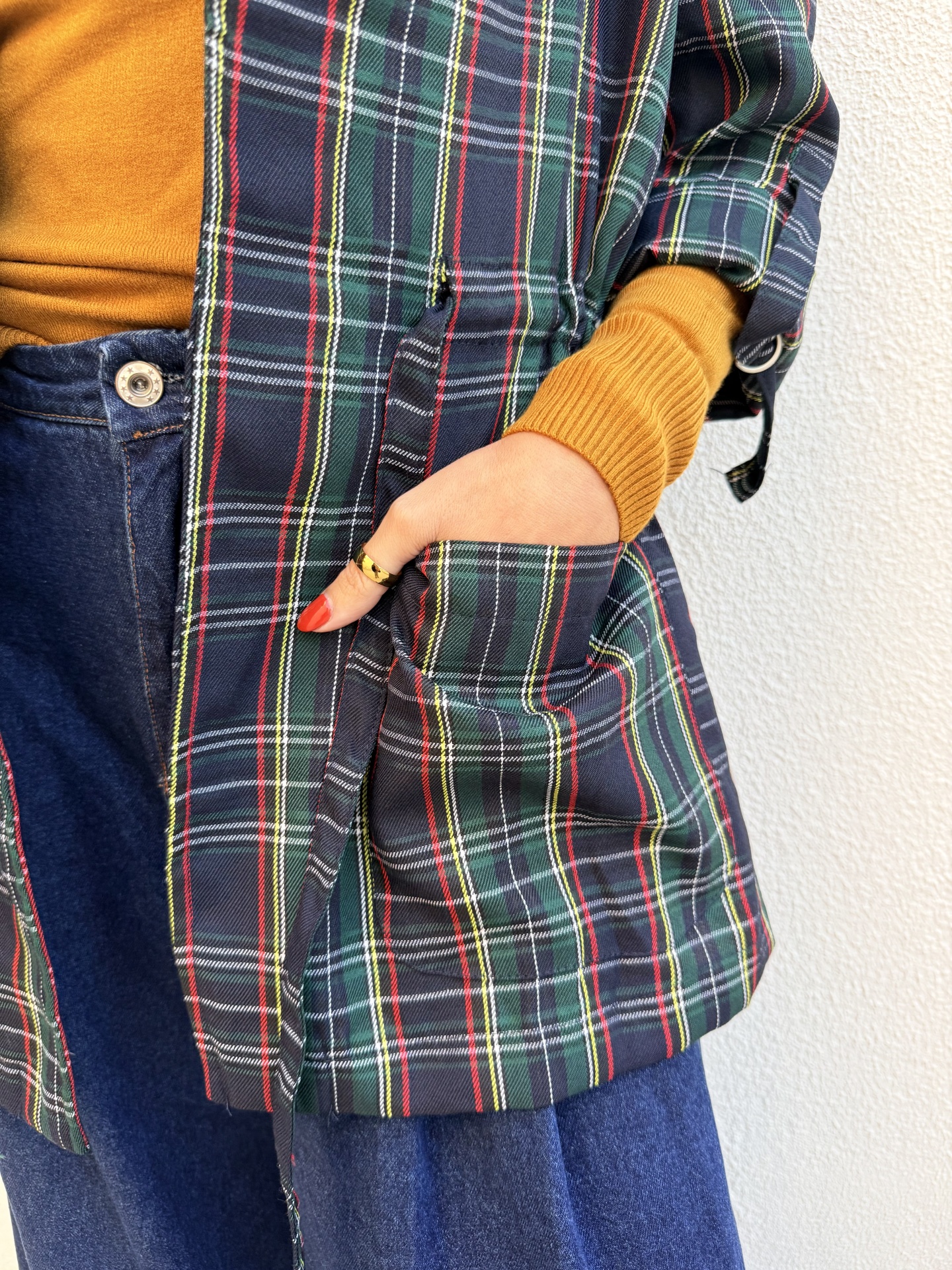Close-up de camisa xadrez azul, verde, vermelho, mostarda e calças de ganga azul.