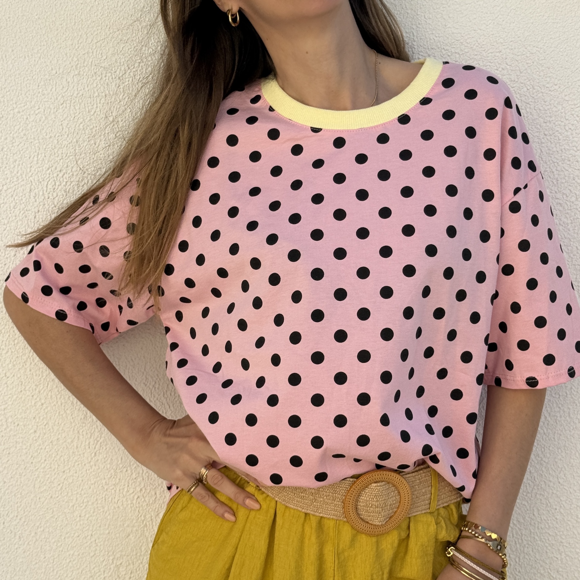 T-shirt rosa com bolinhas pretas e gola amarela, calças amarelas com cinto bege e acessórios dourados