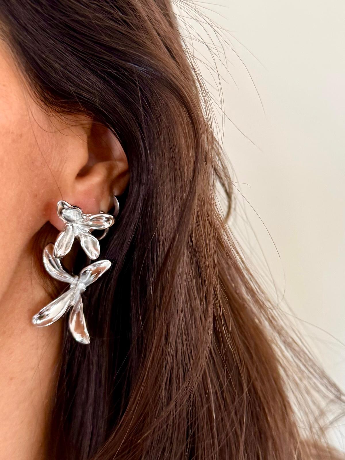 Brinco prateado em forma de folhas ou pétalas num fundo claro