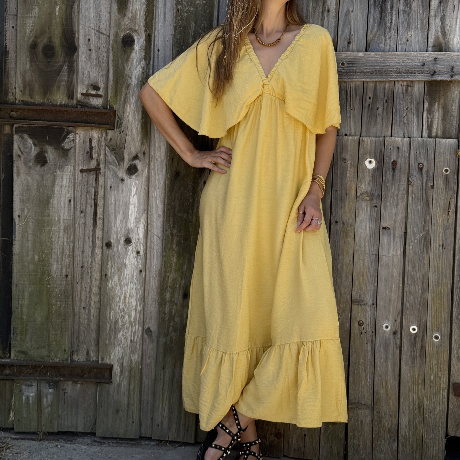 Vestido amarelo leve com decote em V e babados usado por pessoa perto de porta de madeira