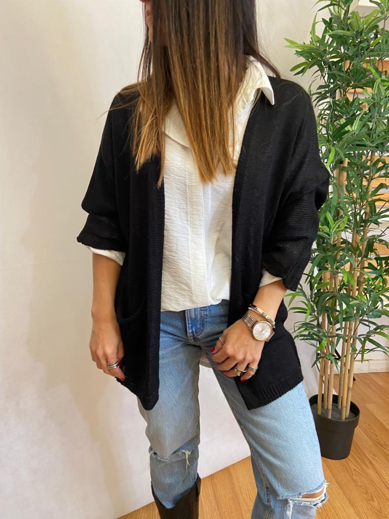 Mulher com camisola preta de malha e camisa branca, calças de ganga rasgadas, em sala com planta em vaso preto