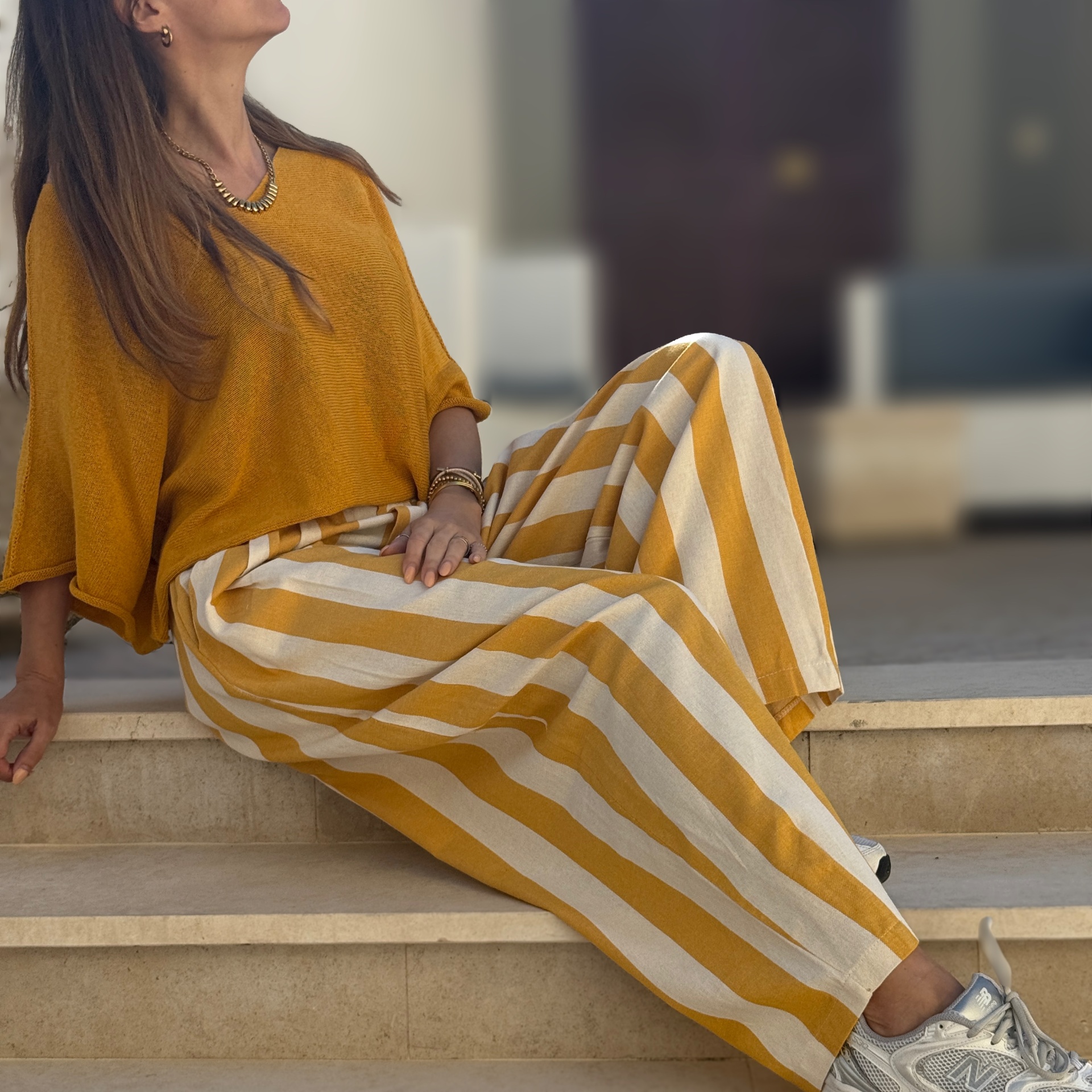 Mulher com camisola laranja e calças com riscas largas em tons laranja e creme, a usar sapatilhas cinza