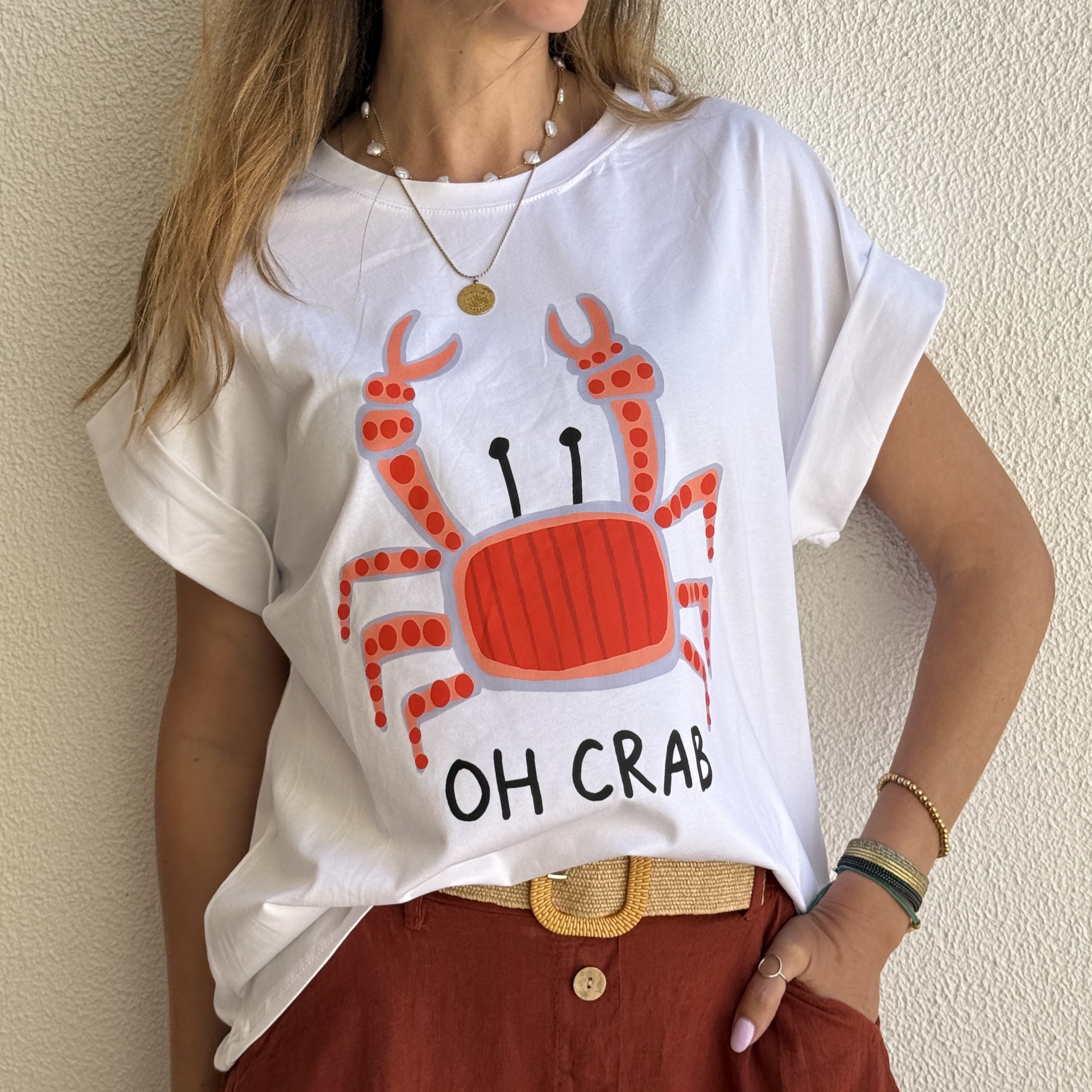 T-shirt branca com caranguejo vermelho estampado e texto OH CRAB combinada com saia castanha e cinto amarelo.