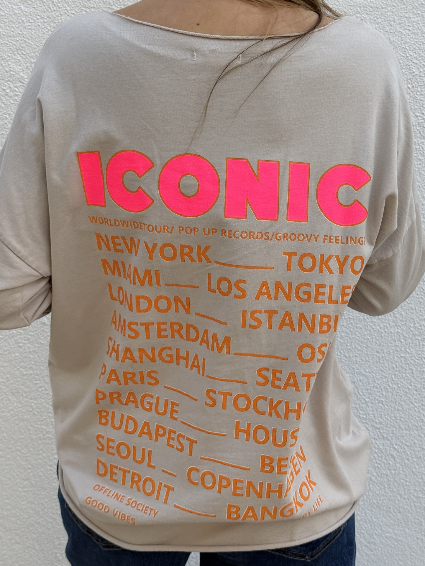 Camisola bege com texto colorido e nomes de cidades nas costas