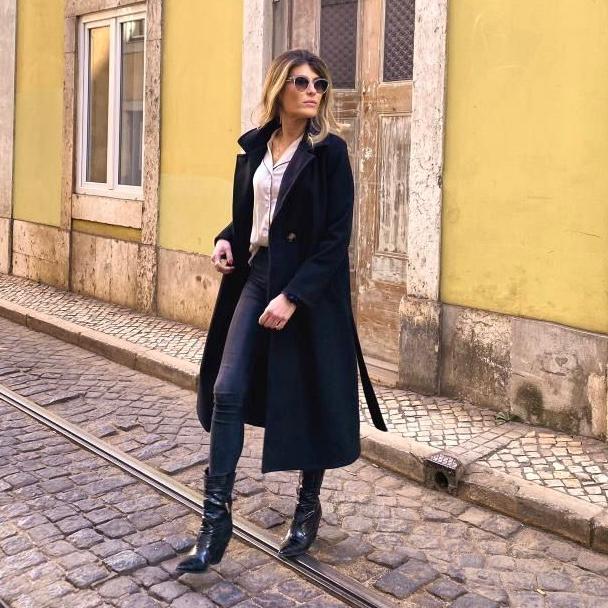 Mulher com casaco preto comprido, calças pretas e botas pretas na rua