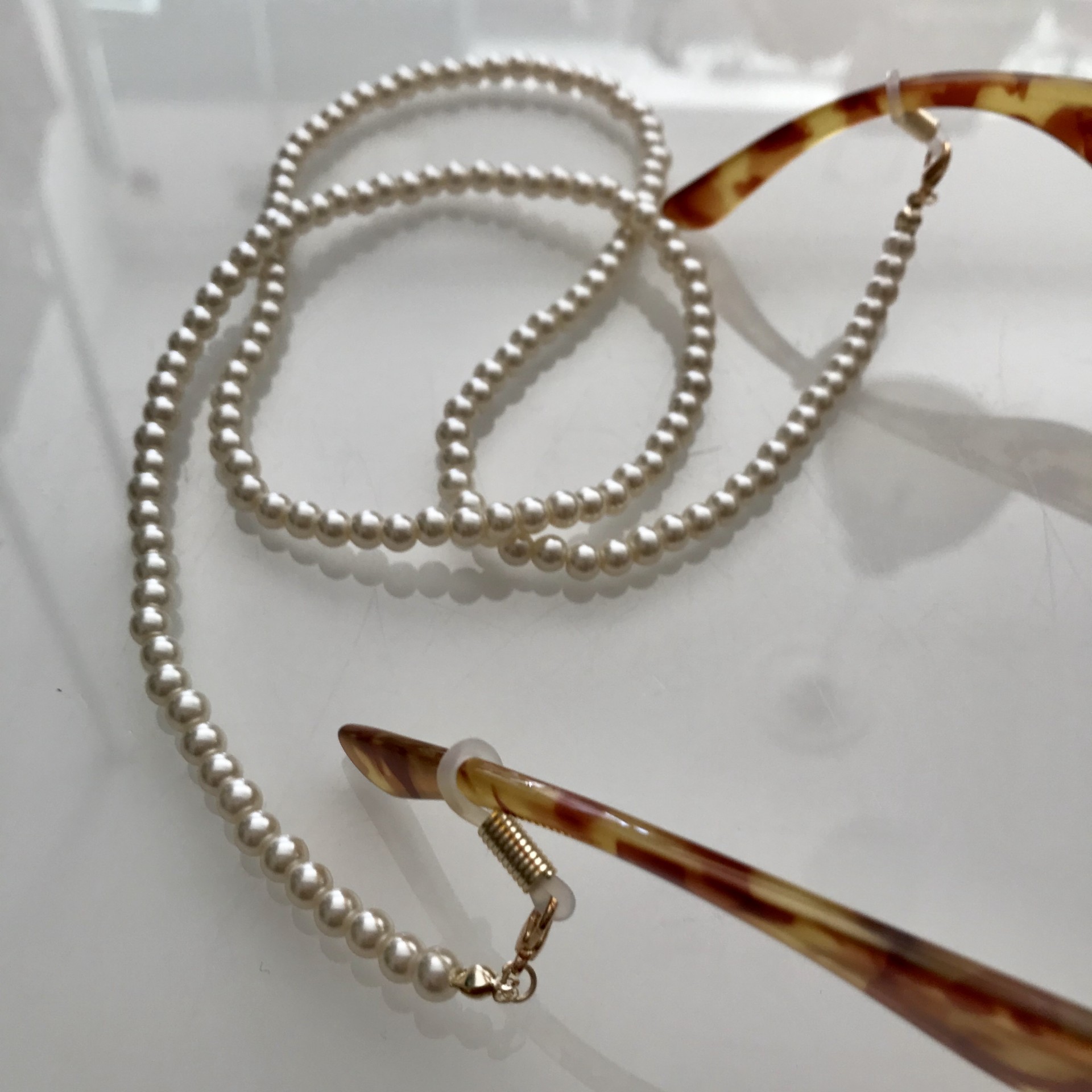 Cordão para óculos com pérolas brancas e armação de óculos castanha com padrão tartaruga