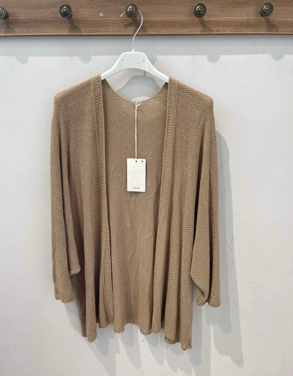 Cardigan castanho de malha pendurado em cabide branco contra parede branca