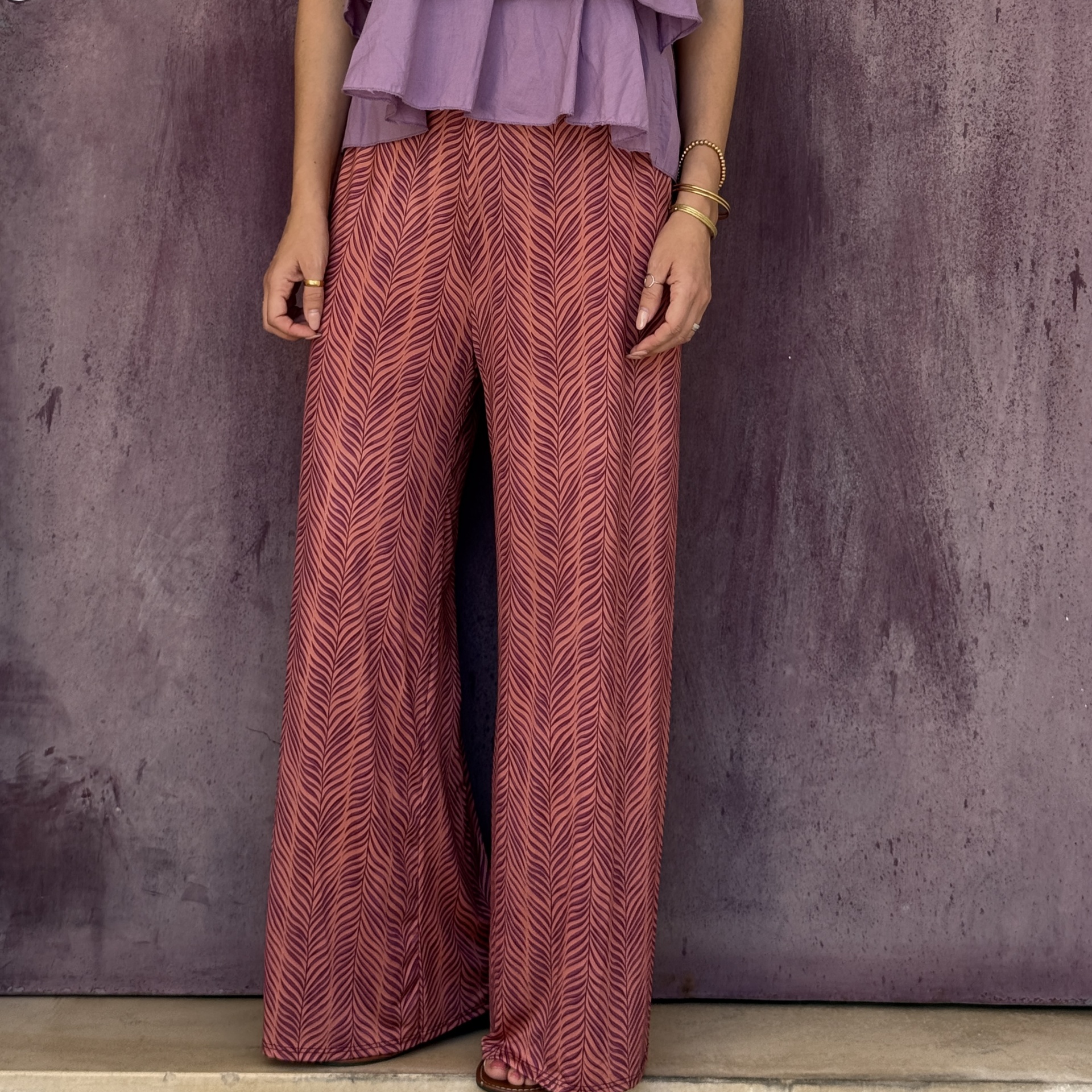 Calças largas rosa com padrão ziguezague e blusa lilás com pulseiras douradas.