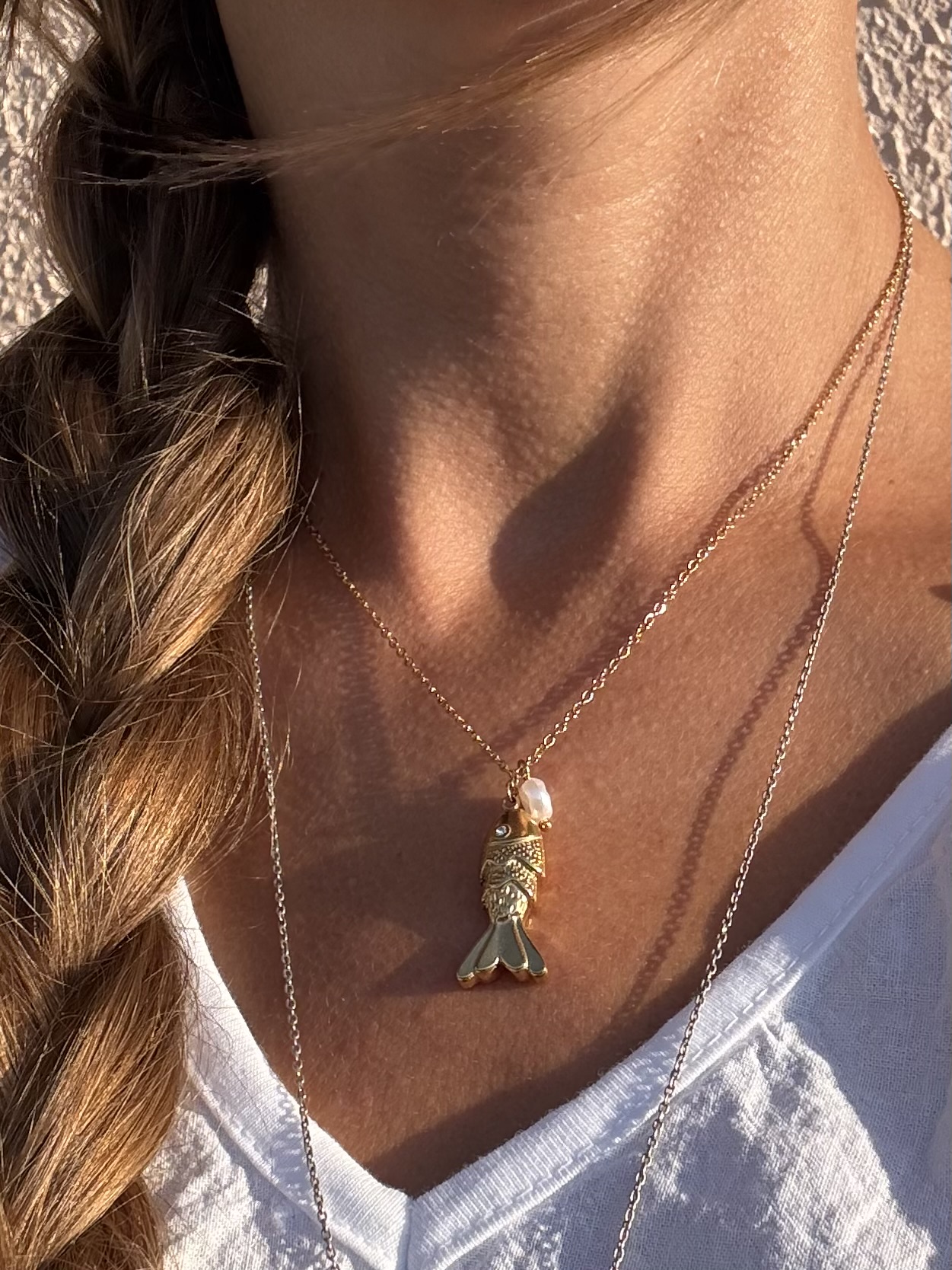 Colar dourado com pendente de peixe e pérola ao pescoço