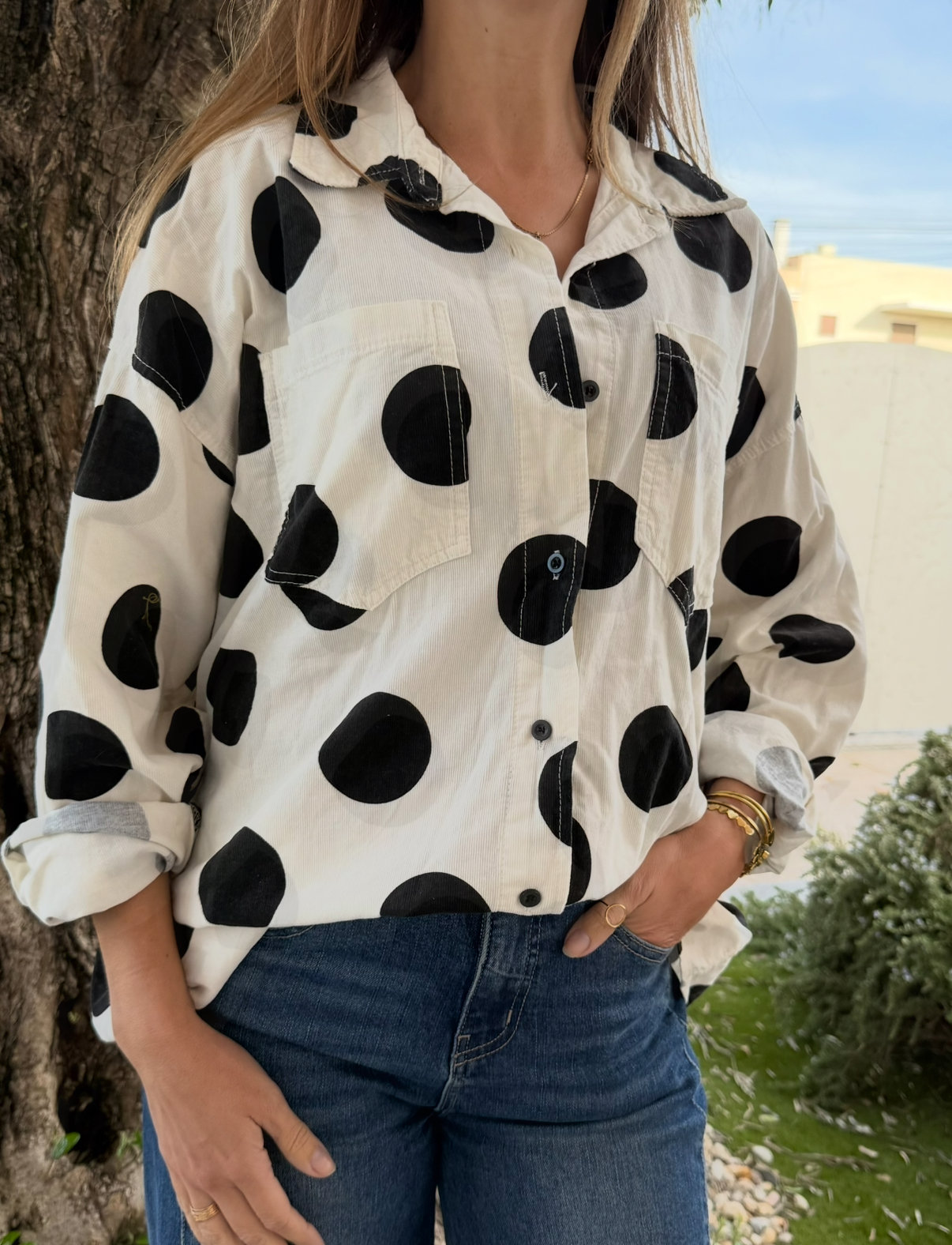 Camisa branca com círculos pretos grandes em ambiente exterior junto a uma árvore e vegetação