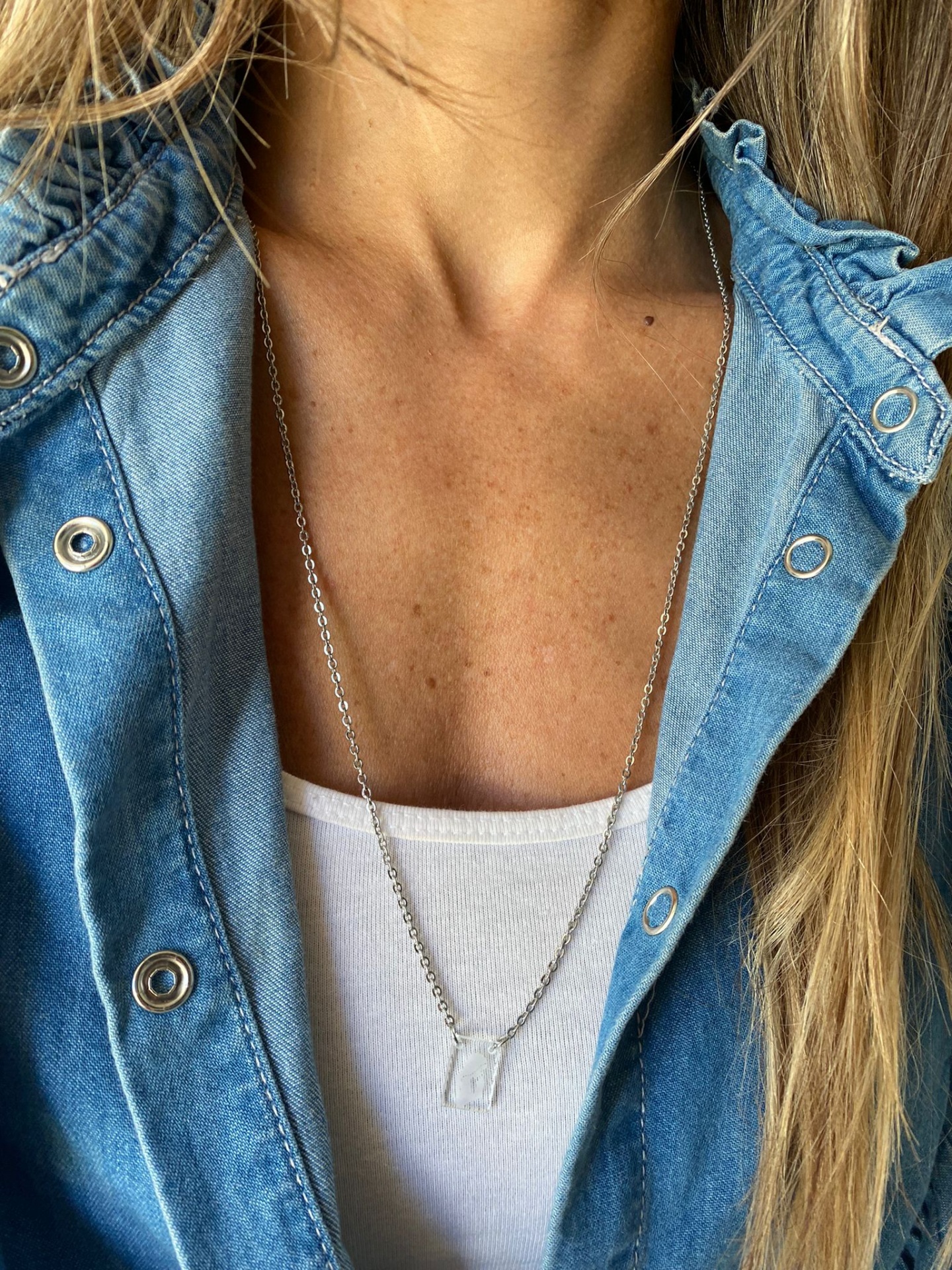 Colar prateado com pendente transparente usado sobre camisola branca e casaco azul de ganga