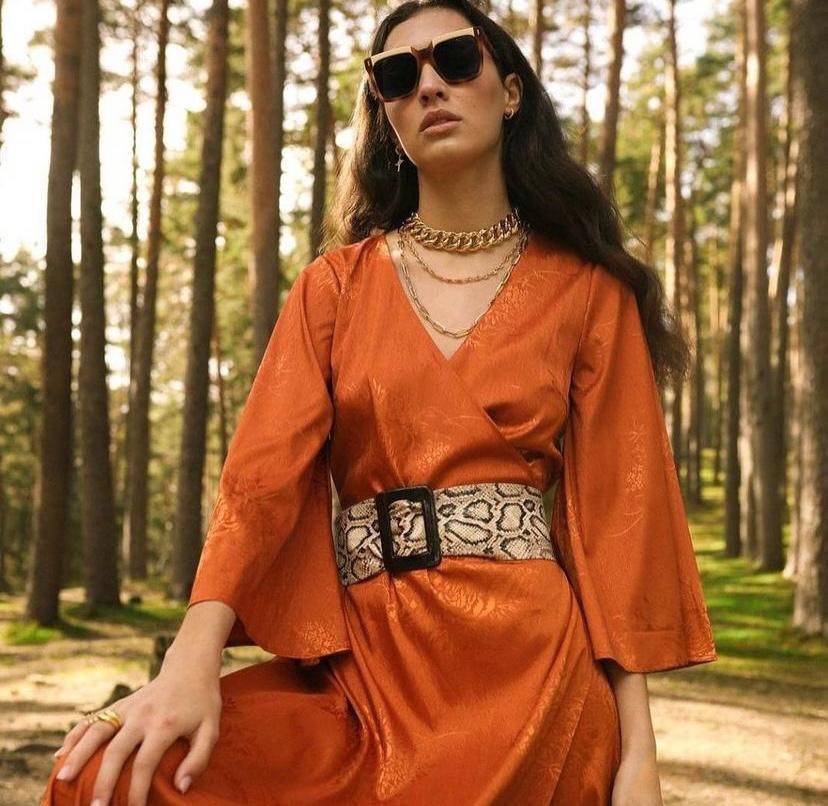 Mulher com vestido alaranjado brilhante e cinto largo estampado de cobra em floresta
