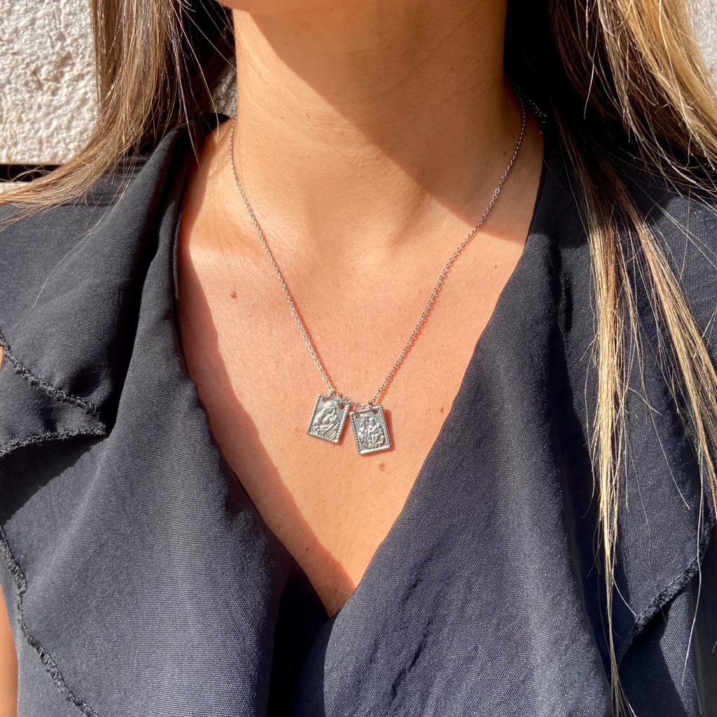 Colar prateado com duas placas retangulares penduradas no pescoço de uma pessoa com blusa preta