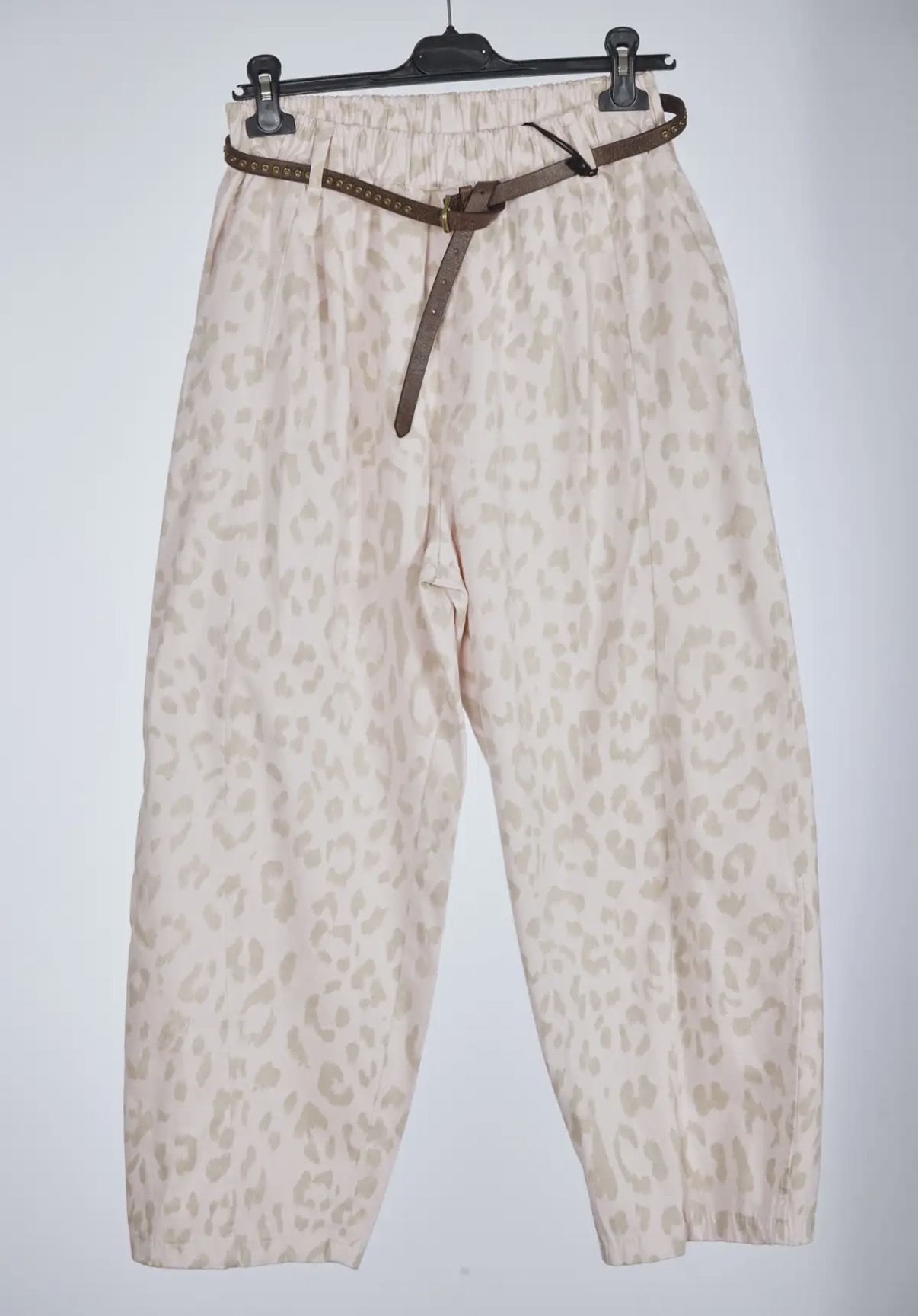 Calças largas bege com padrão animal e cinto castanho no cabide