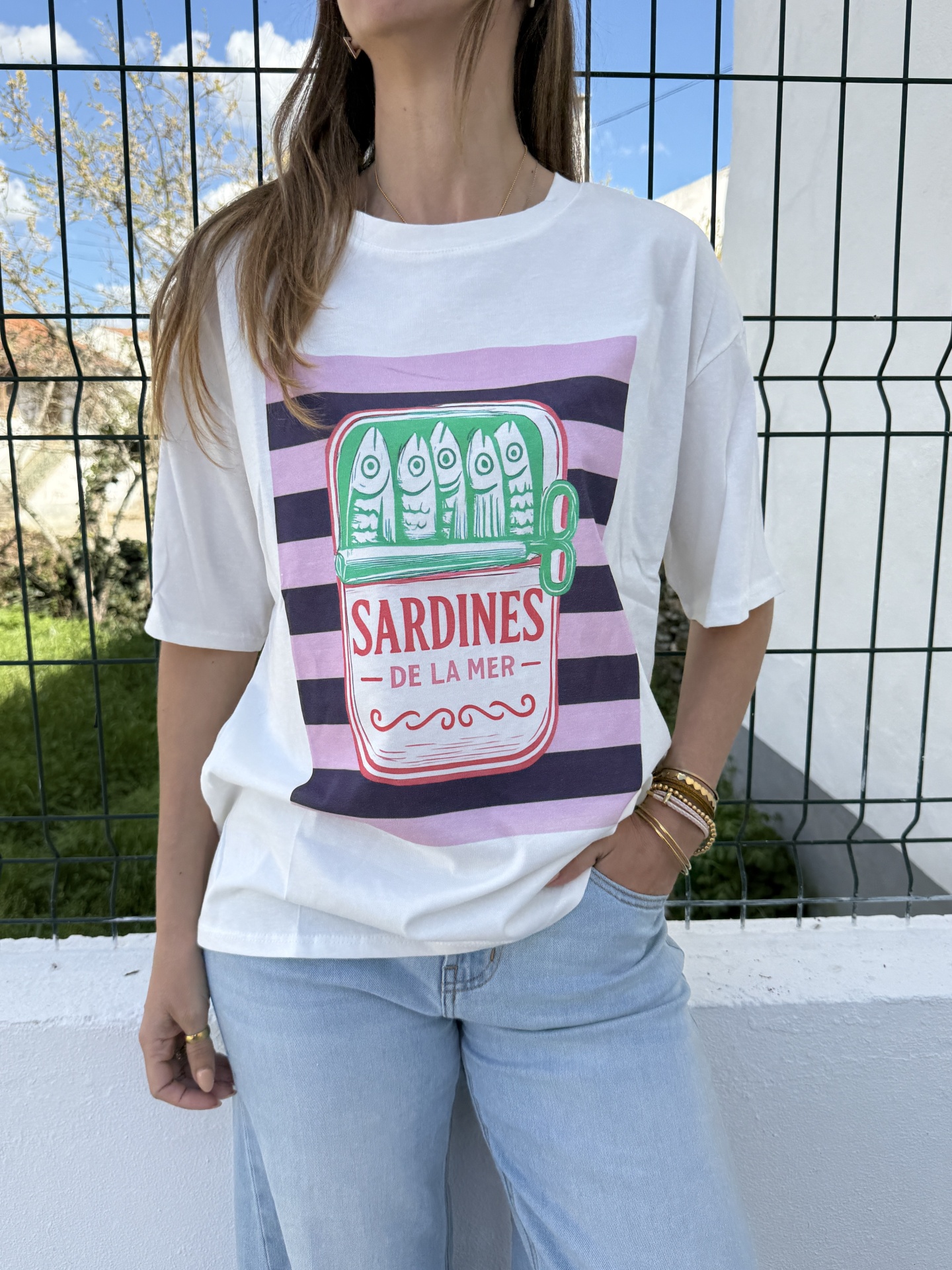 T-shirt branca com estampa de sardinhas numa lata colorida e calças de ganga claras.