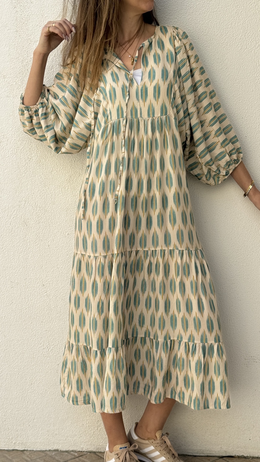 Vestido comprido bege com padrão geométrico verde, mangas largas e gola com cordão.