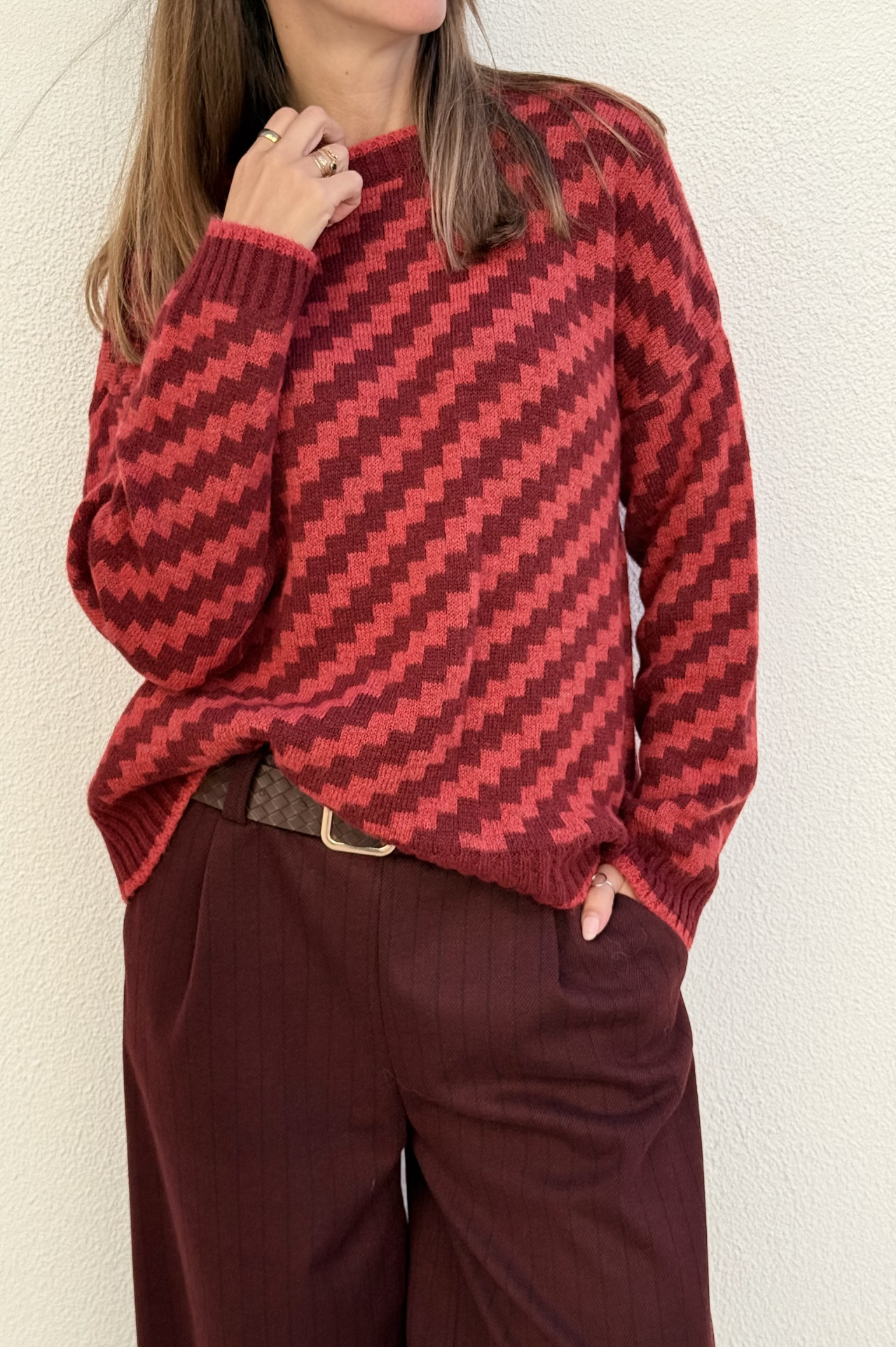 Camisola de malha vermelha e vinho com padrão ziguezague, calças castanhas e cinto castanho com fivela dourada