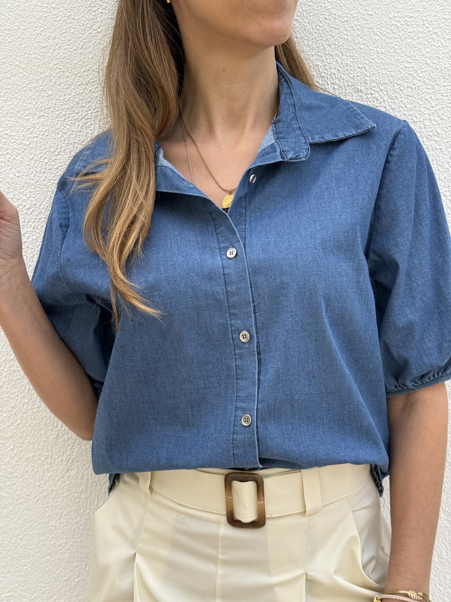 Blusa azul de manga curta com botões e gola clássica, calças bege com cinto de fivela quadrada castanha