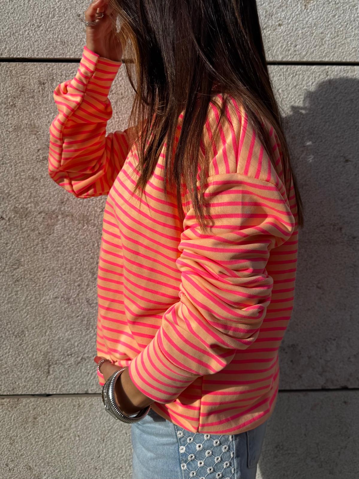 Pessoa com sweatshirt de riscas rosa e laranja e calças de ganga azuis com bordados