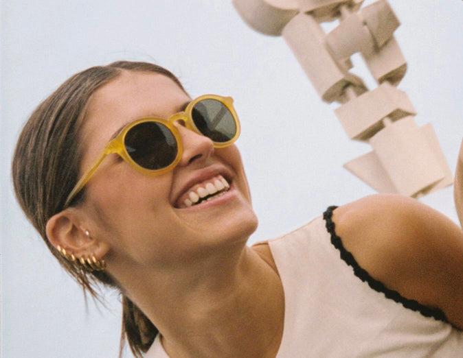 Mulher sorridente a usar óculos de sol amarelos com fundo neutro